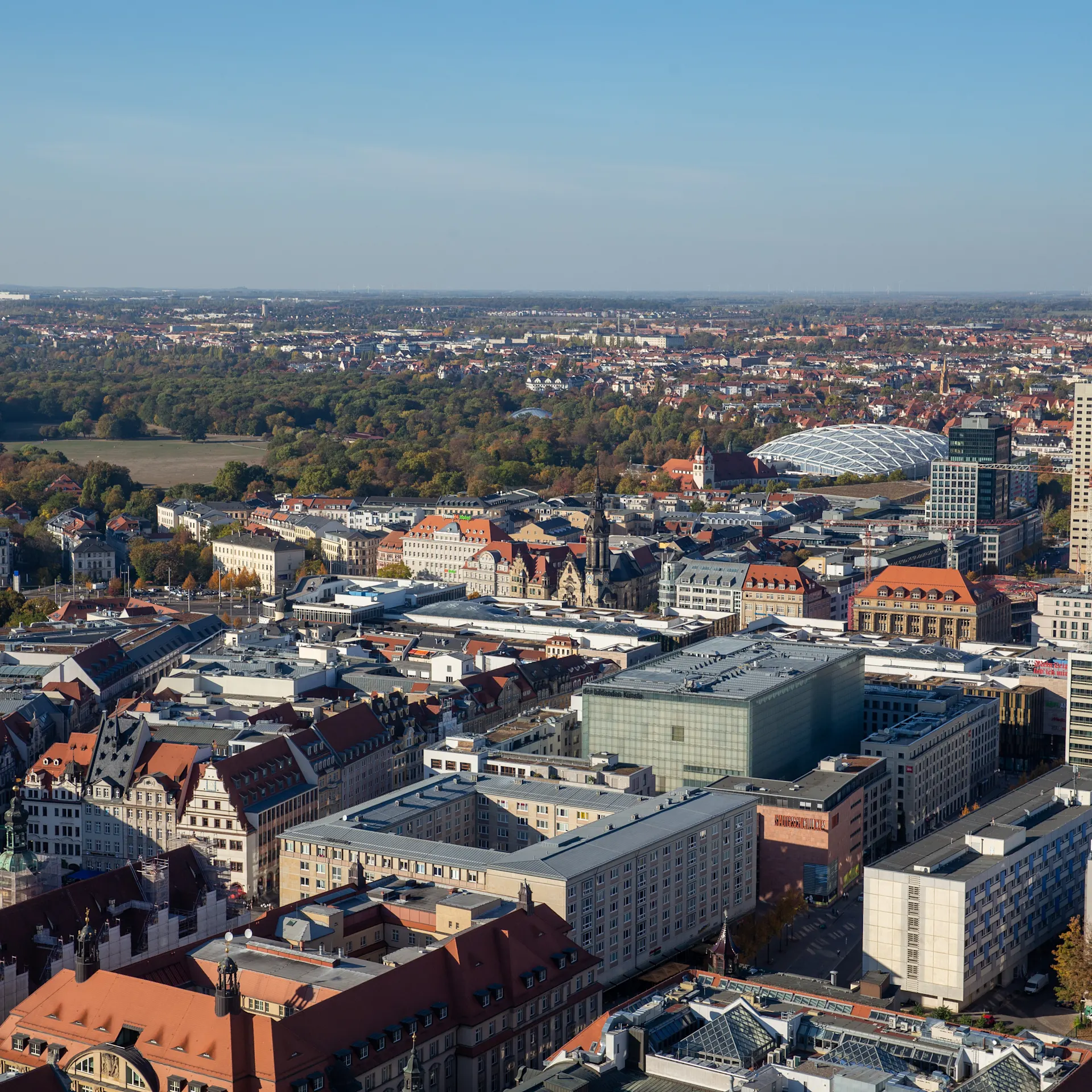 Stadtansicht mit vielen Gebäuden, roten Dächern und Parkanlagen im Hintergrund.