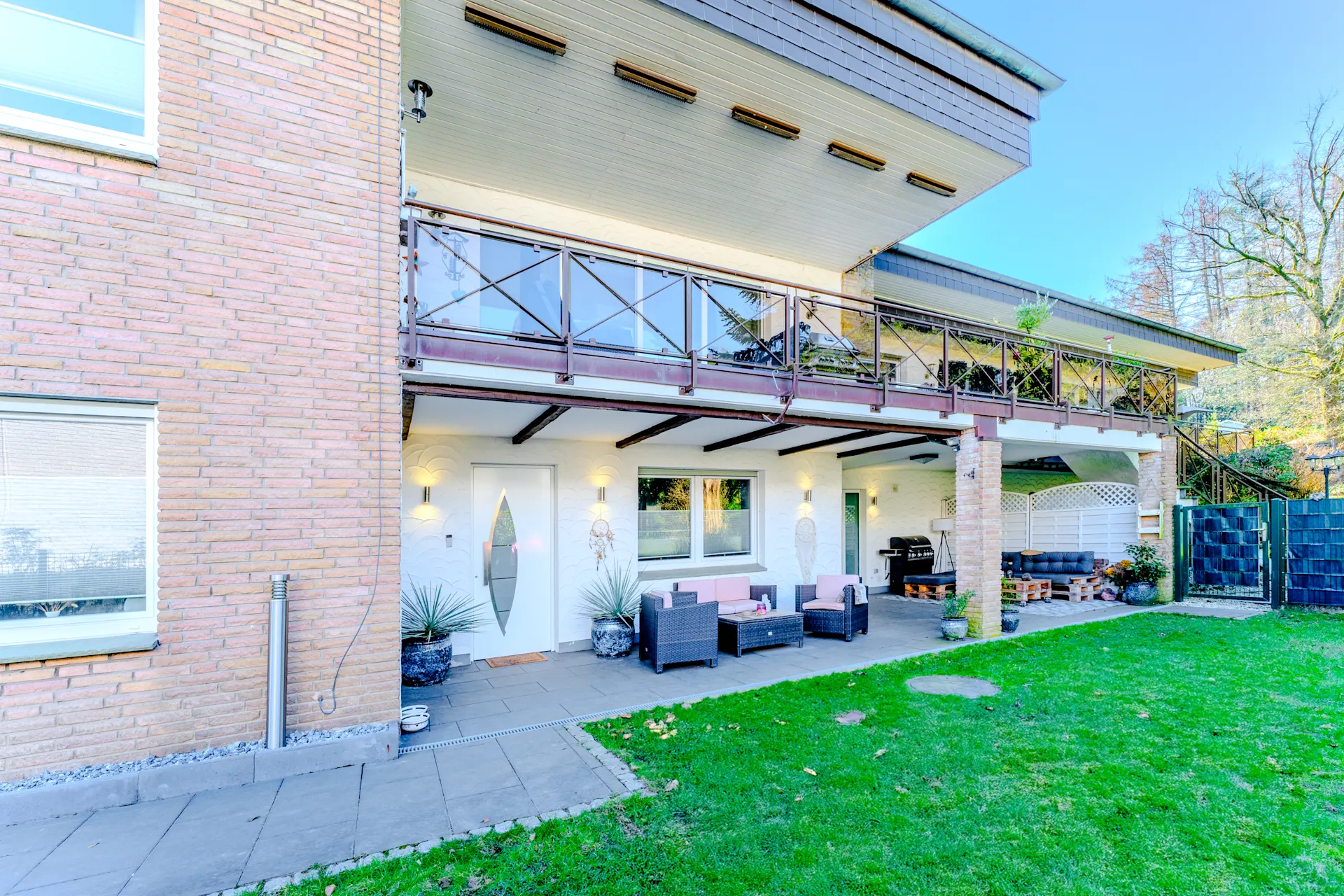 Terrasse eines Wohnhauses mit Sitzmöbeln, Grill und begrünter Gartenfläche.