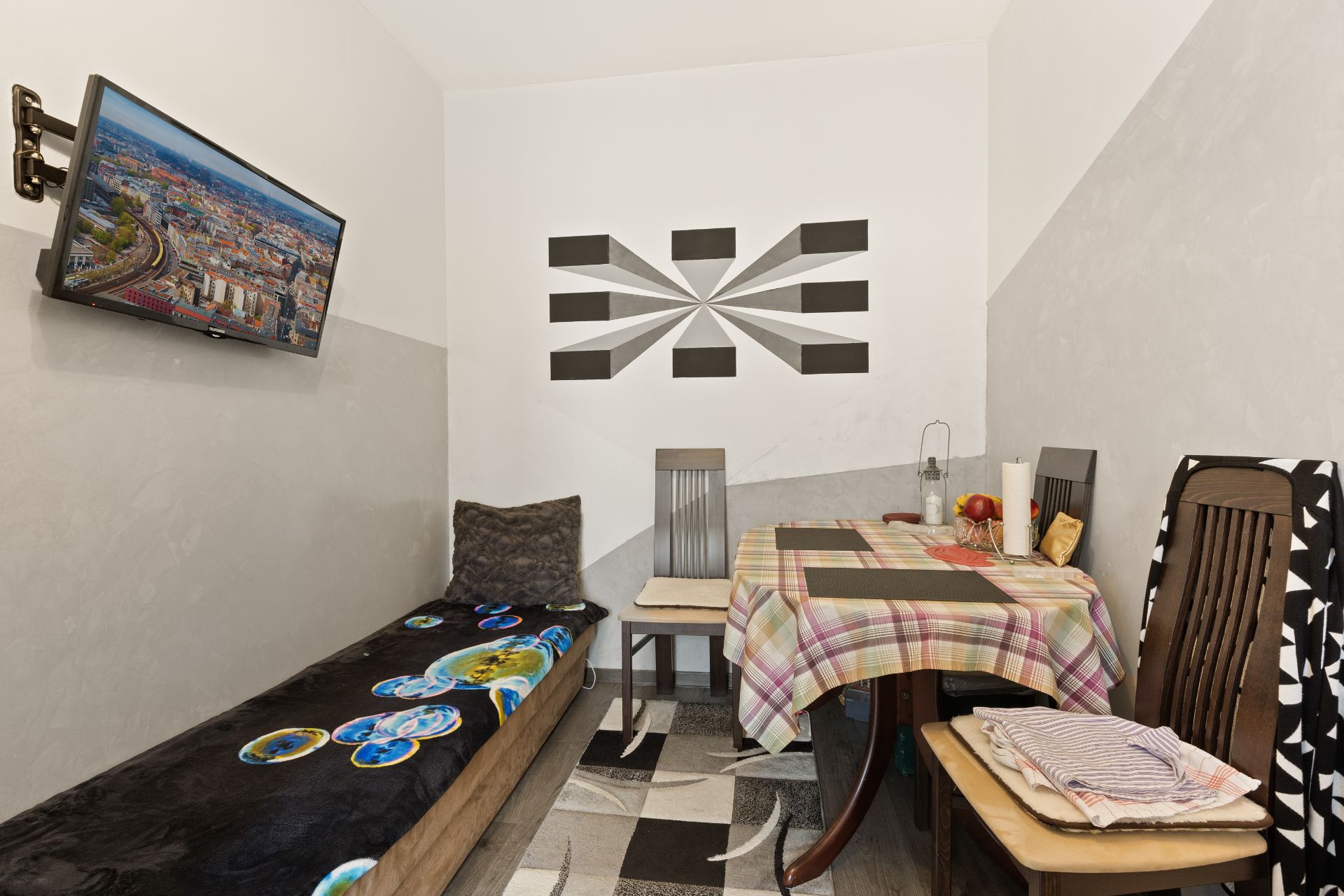 Kleiner Raum mit Tisch, Stühlen, Sofa, Wandbild und Fernseher an der Wand.