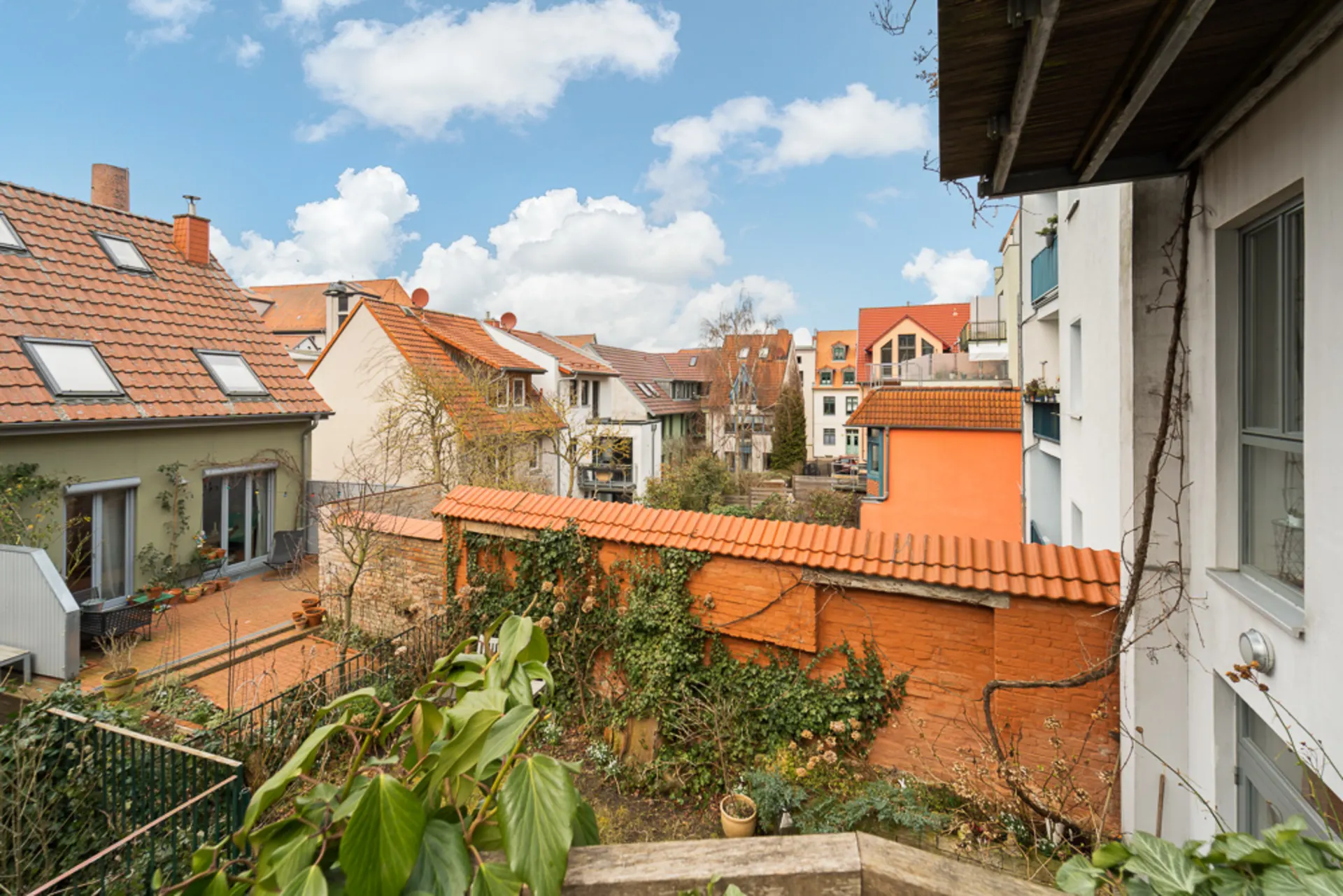 Blick auf Wohnhäuser mit roten Dächern und einen begrünten Innenhof bei Tageslicht.