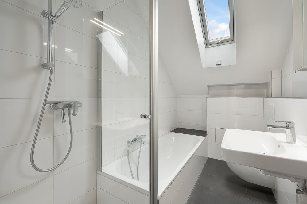 Modernes Badezimmer mit Badewanne, Dusche, Waschbecken und Fenster im Dach.