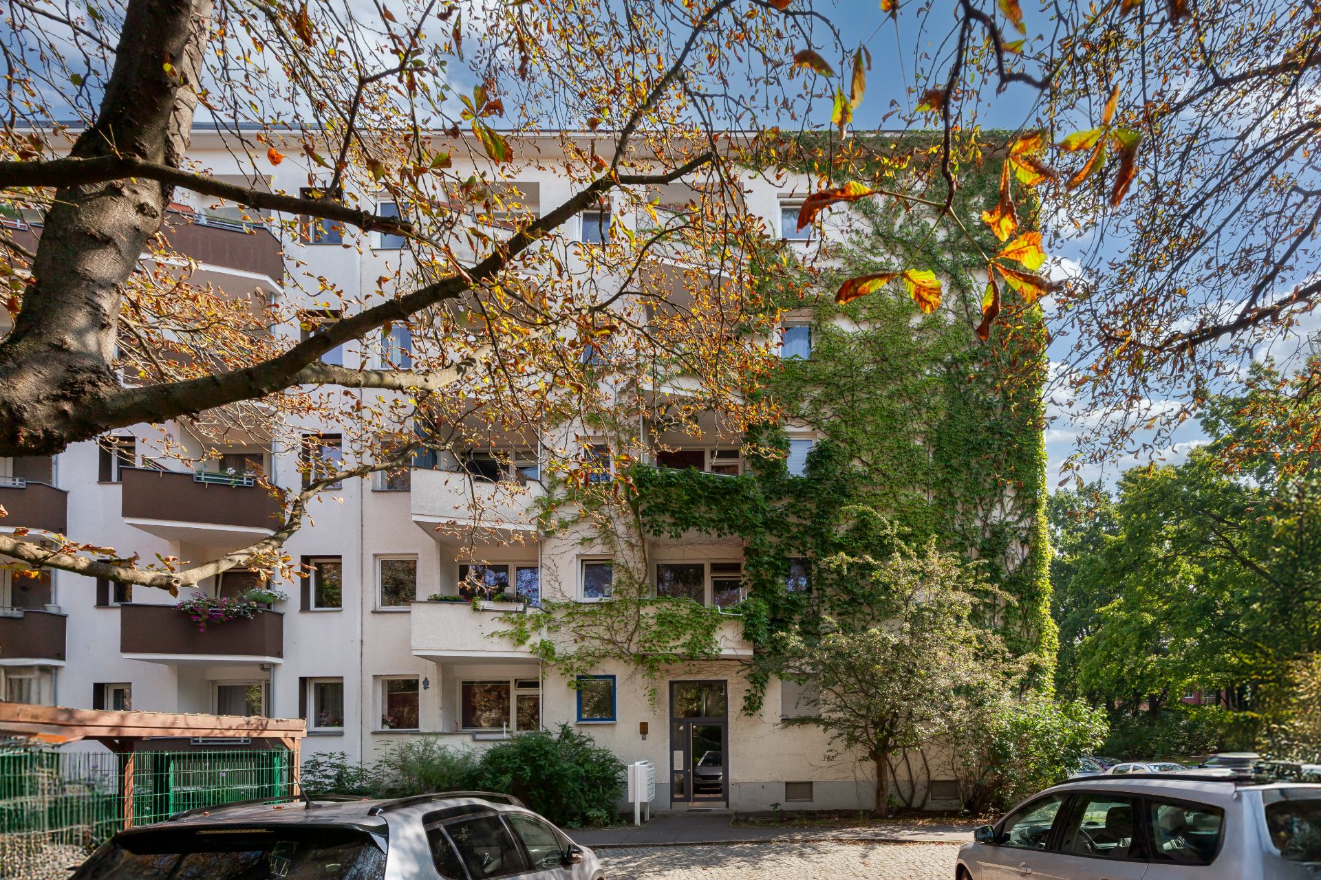 Mehrfamilienhaus mit Balkonen, bepflanzter Fassade und geparkten Autos davor.