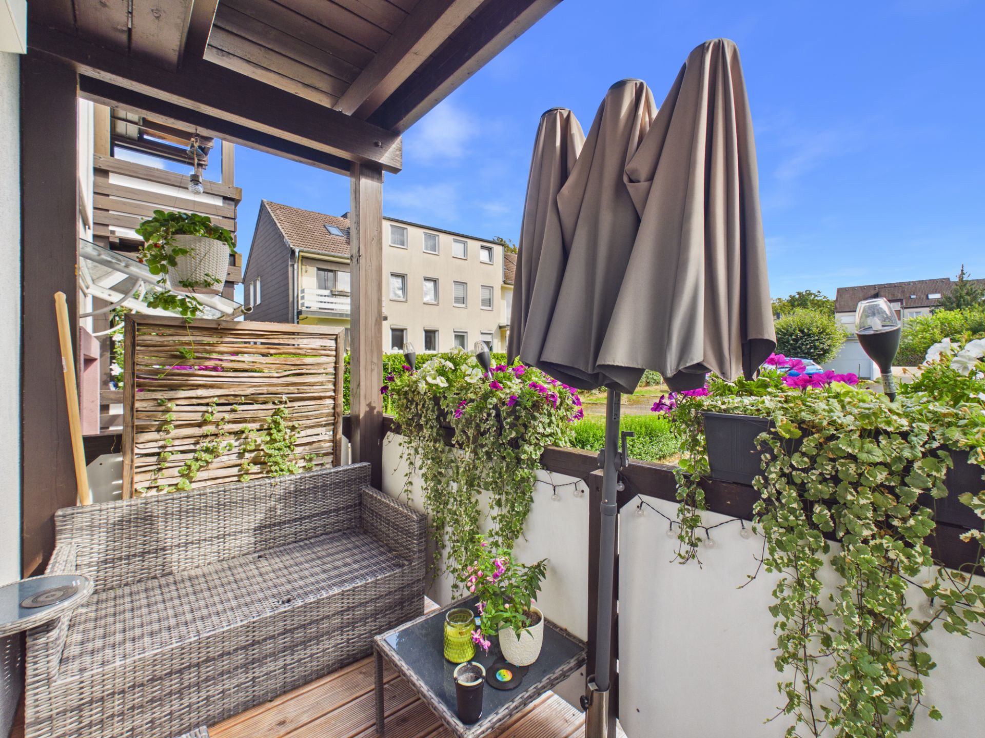 Überdachter Balkon mit Sitzbank, Pflanzen, Tisch und geschlossenem Sonnenschirm.