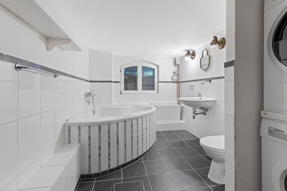 Modernes Badezimmer mit Eckbadewanne, Waschbecken, Toilette und Stapelwaschmaschine.