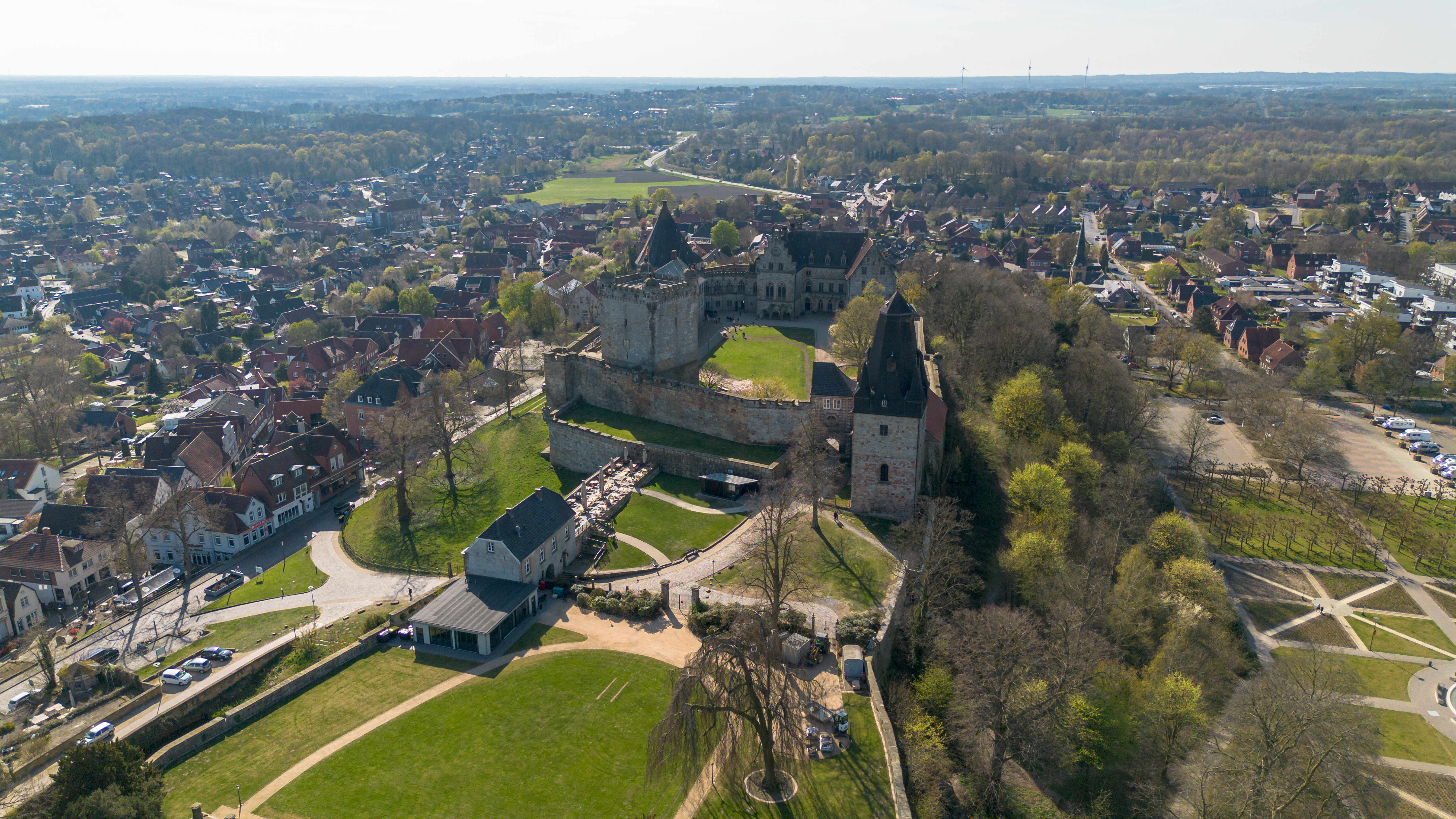Luftaufnahme einer Burg mit mehreren Gebäuden und viel Grünfläche, umgeben von einer Stadt.