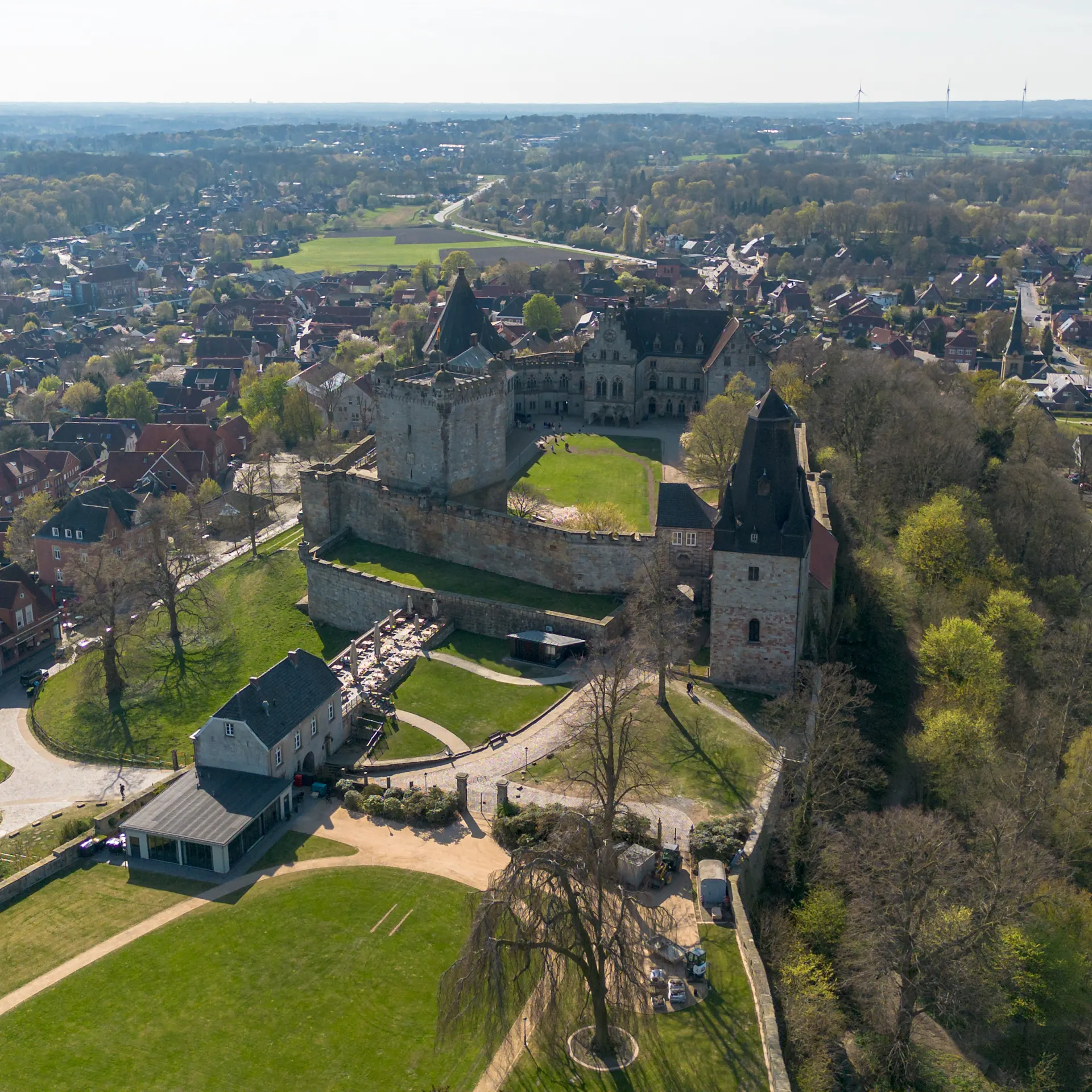 Luftaufnahme einer Burg mit mehreren Gebäuden und viel Grünfläche, umgeben von einer Stadt.