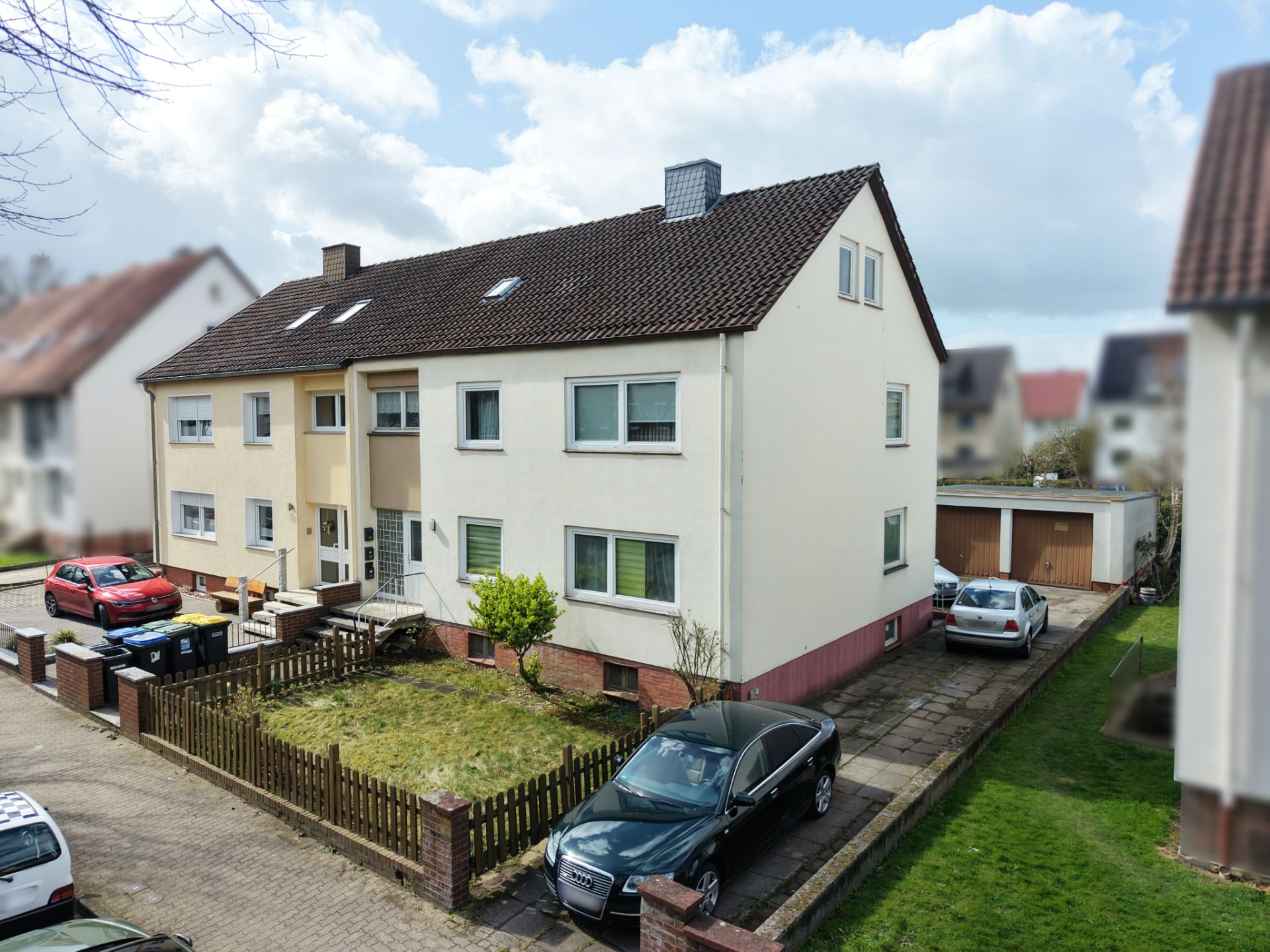Zweistöckiges Wohnhaus mit Garten, Einfahrt und mehreren geparkten Autos.