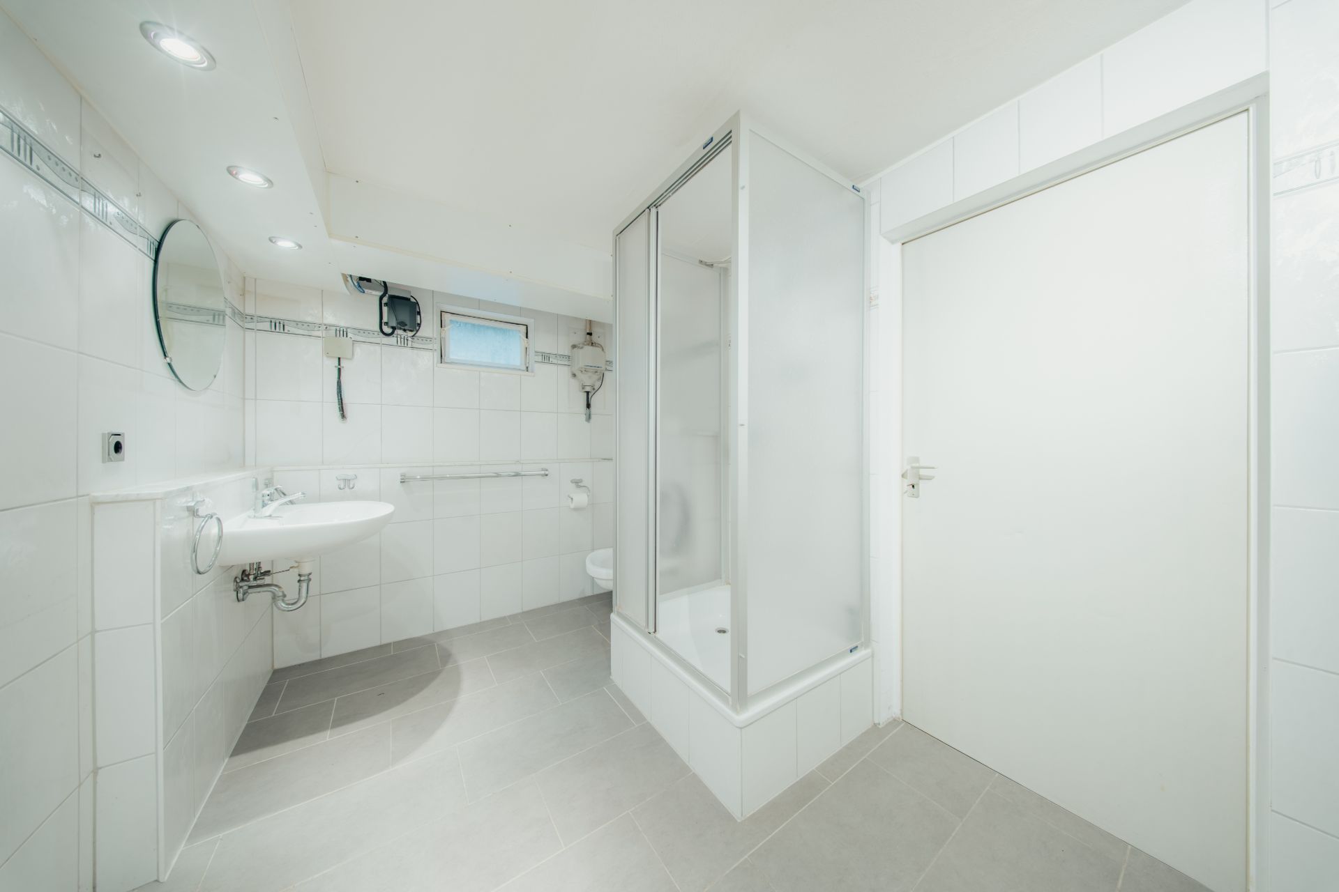 Helles Badezimmer mit Dusche, Waschbecken, Spiegel und weiß gefliesten Wänden.