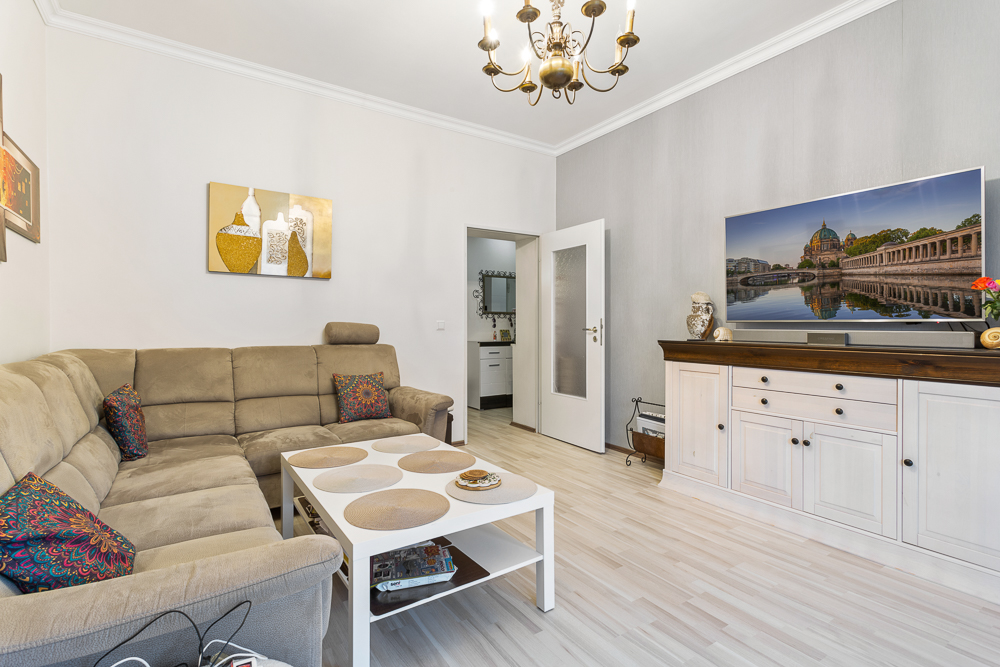 Wohnzimmer mit Ecksofa, Couchtisch, TV auf Kommode und Wandbildern.