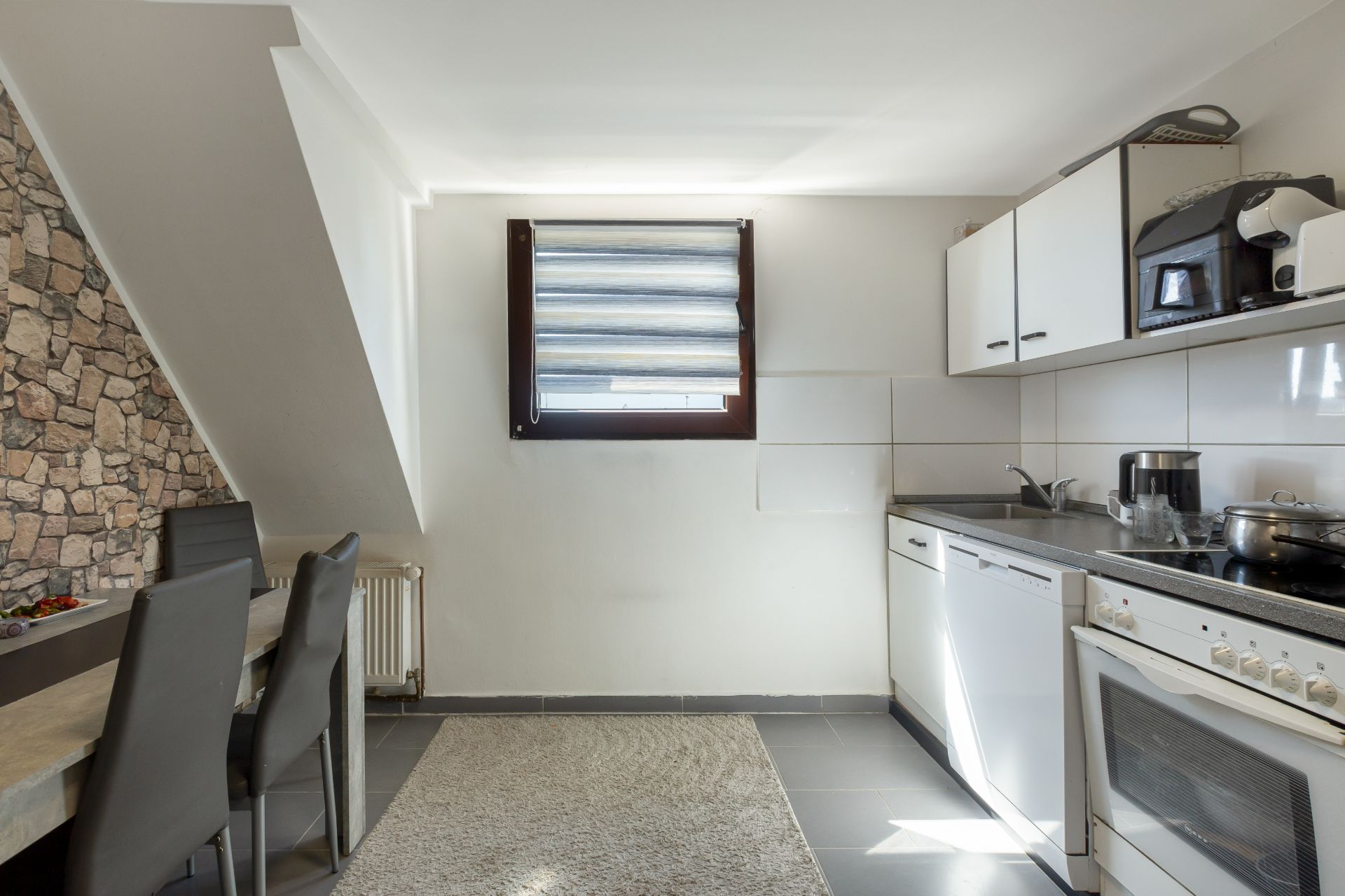 Helle Küche mit Esstisch, Stühlen, Teppich, Fenster und modernen Einbaugeräten.