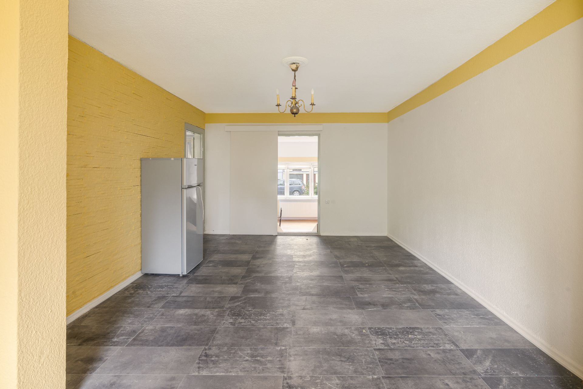 Leerer Raum mit grauem Fliesenboden, gelber Wand und Kühlschrank an der Seite.