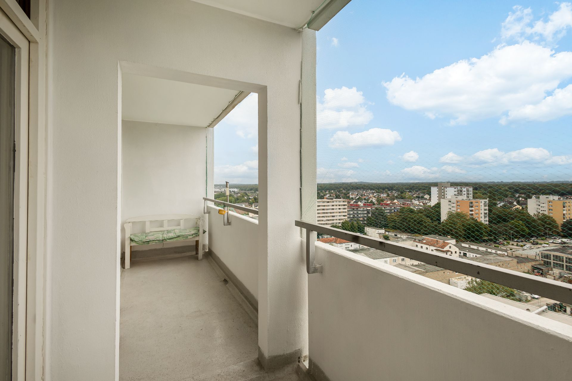 Überdachter Balkon mit Bank, Blick auf Stadt und Wohngebäude im Hintergrund.
