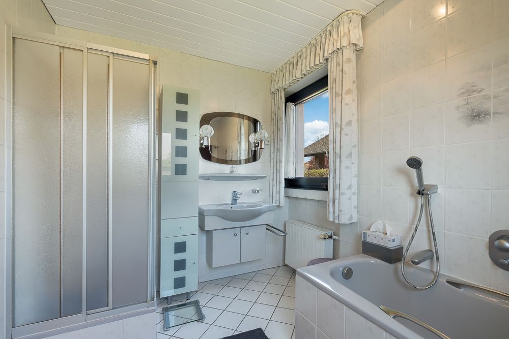 Helles Badezimmer mit Dusche, Badewanne, Waschbecken, Fenster und Spiegelschrank.