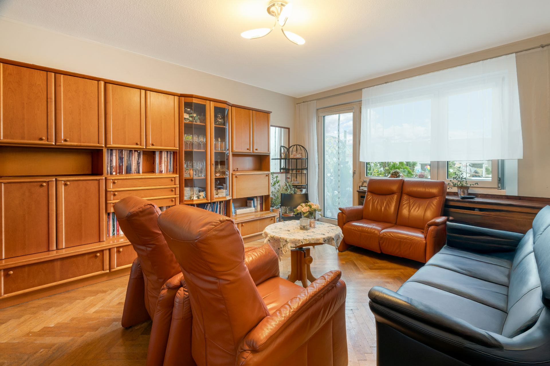 Wohnzimmer mit Ledersesseln, Sofa, großem Holzregal und Fenster mit Vorhang.