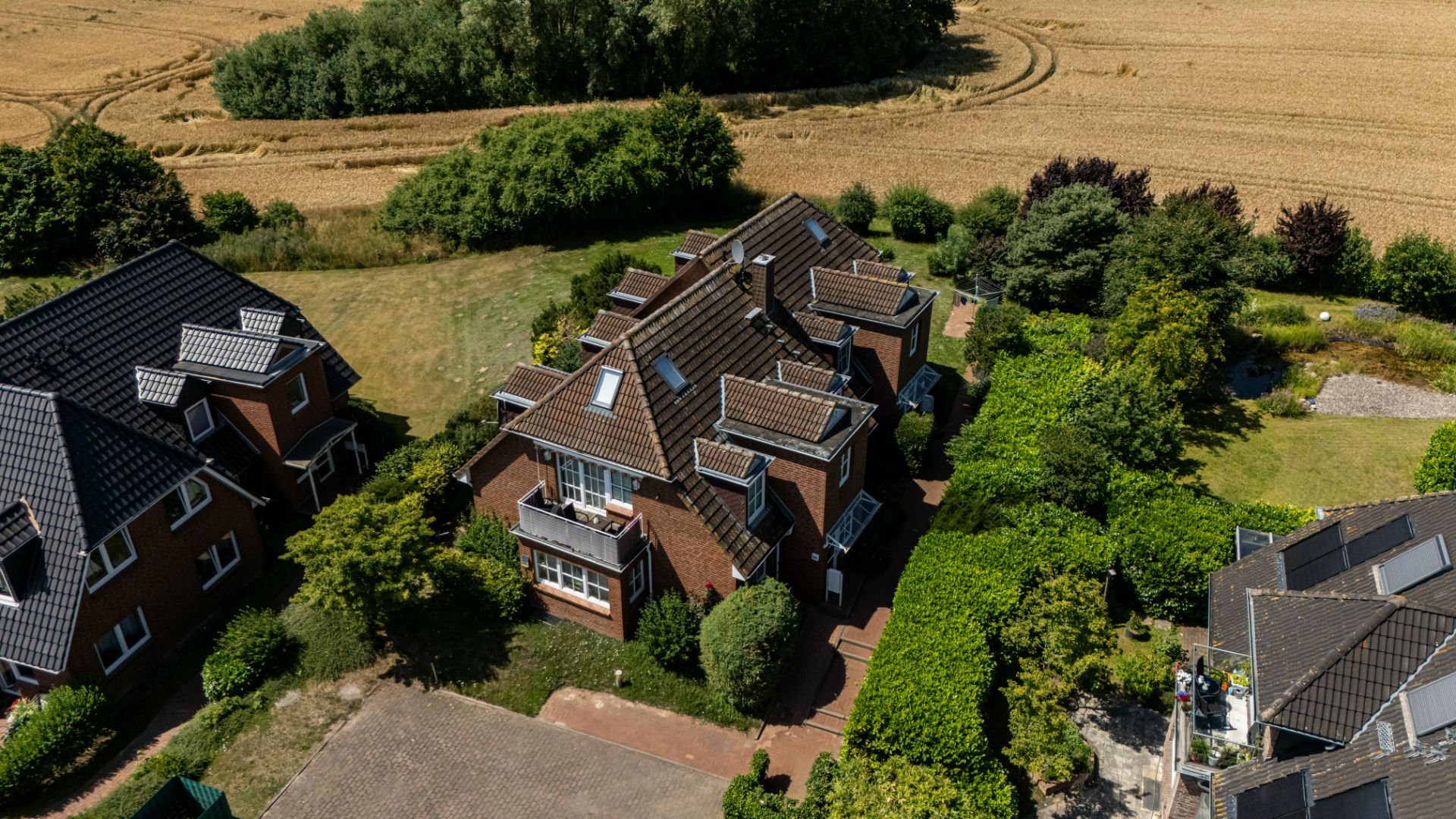 Luftaufnahme eines roten Wohnhauses mit Garten, umgeben von anderen Häusern und Feldern.