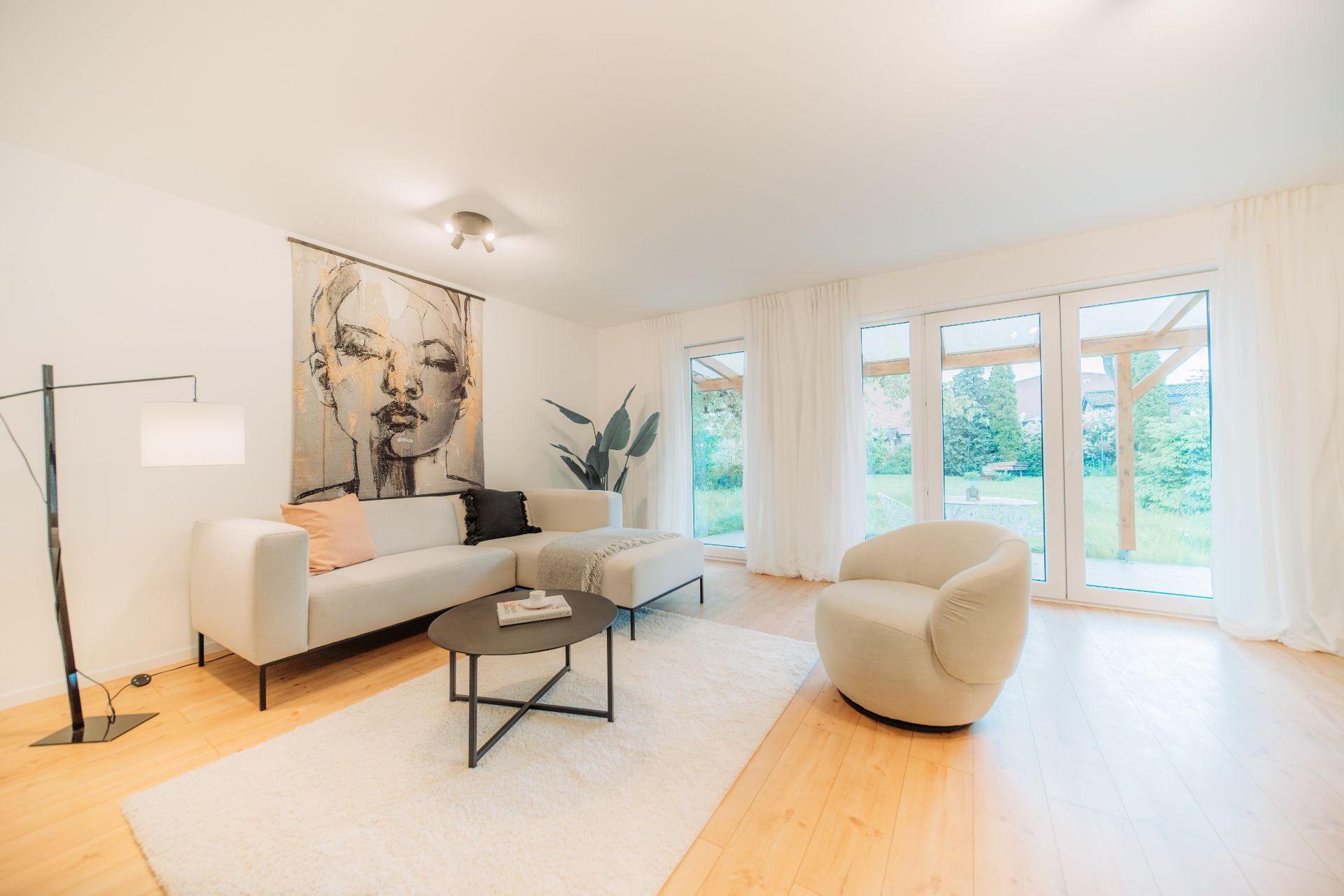 Helles Wohnzimmer mit Sofa, Sessel, großem Fenster, Teppich und moderner Wandkunst.