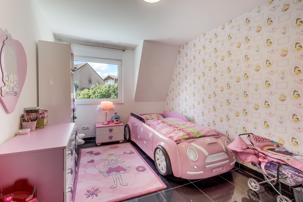 Kinderzimmer mit rosa Autobet, Kommode, Teppich und Fenster, alles in Rosa gehalten.