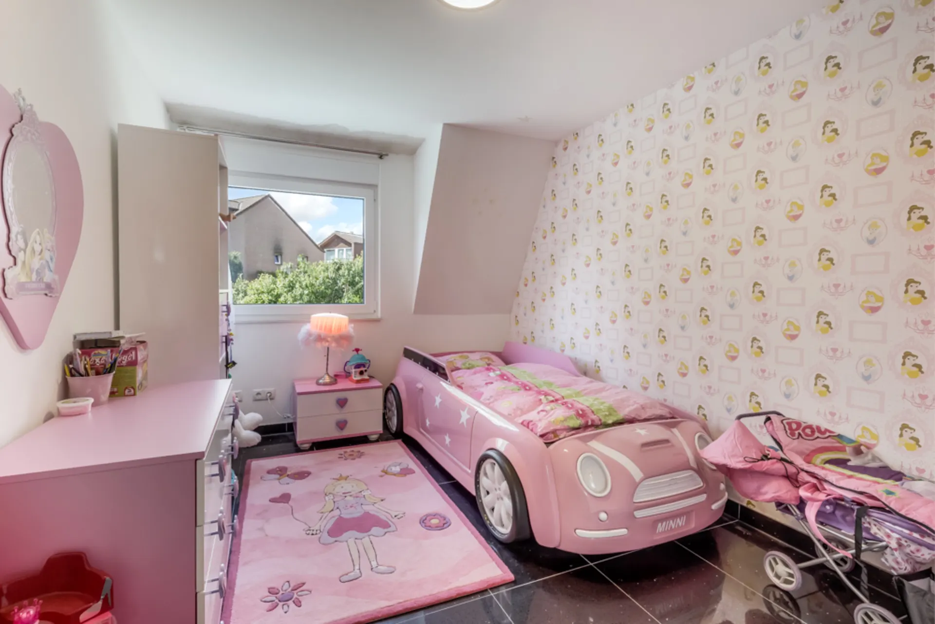 Kinderzimmer mit rosa Autobet, Kommode, Teppich und Fenster, alles in Rosa gehalten.