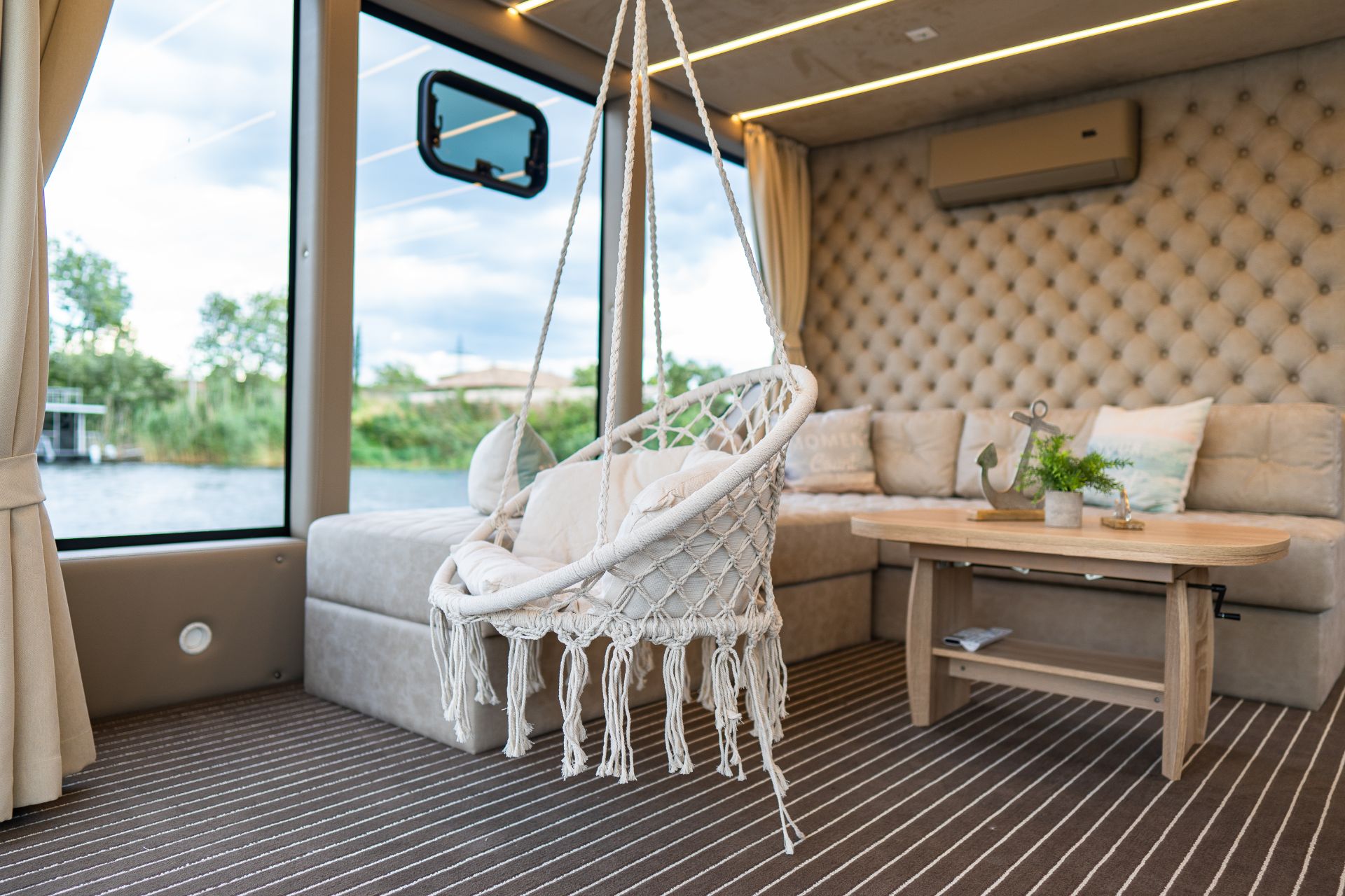 Modernes Wohnzimmer mit Hängesessel, Sofa, Couchtisch und großen Fenstern.