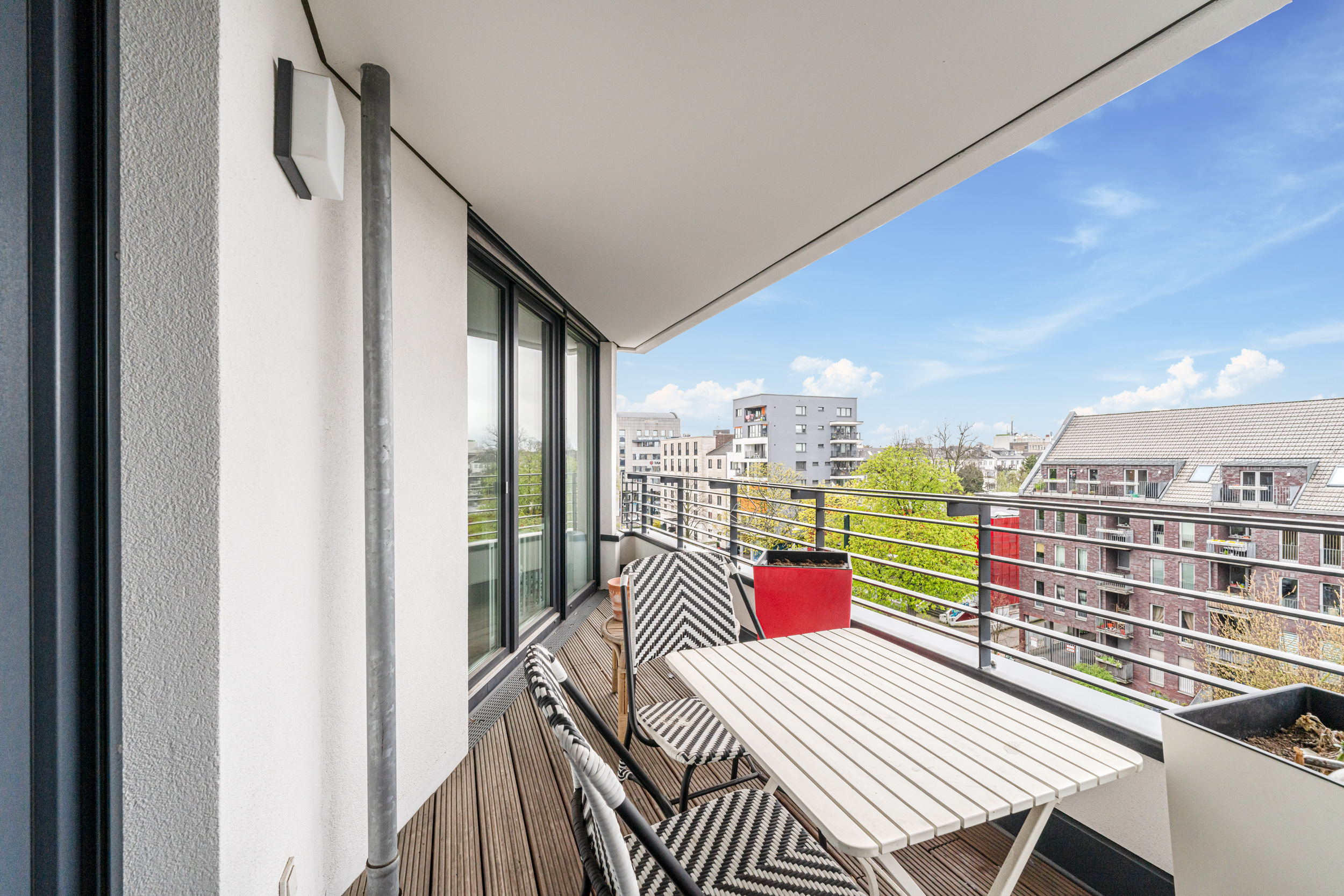 Balkon mit Holzboden, Tisch, Stühlen und Ausblick auf Wohnhäuser.