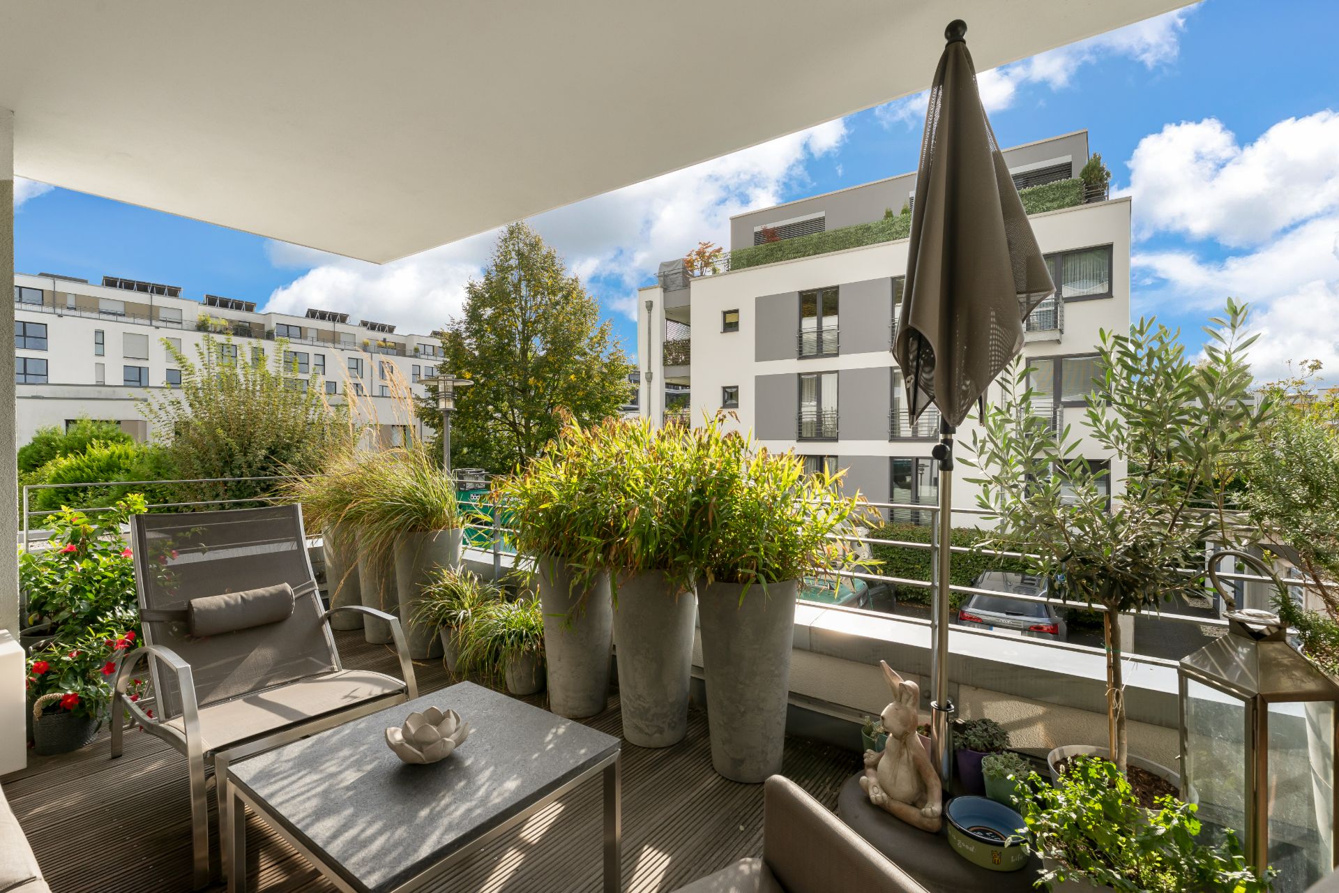 Möblierter Balkon mit Pflanzen und Blick auf moderne Wohngebäude bei Tageslicht.