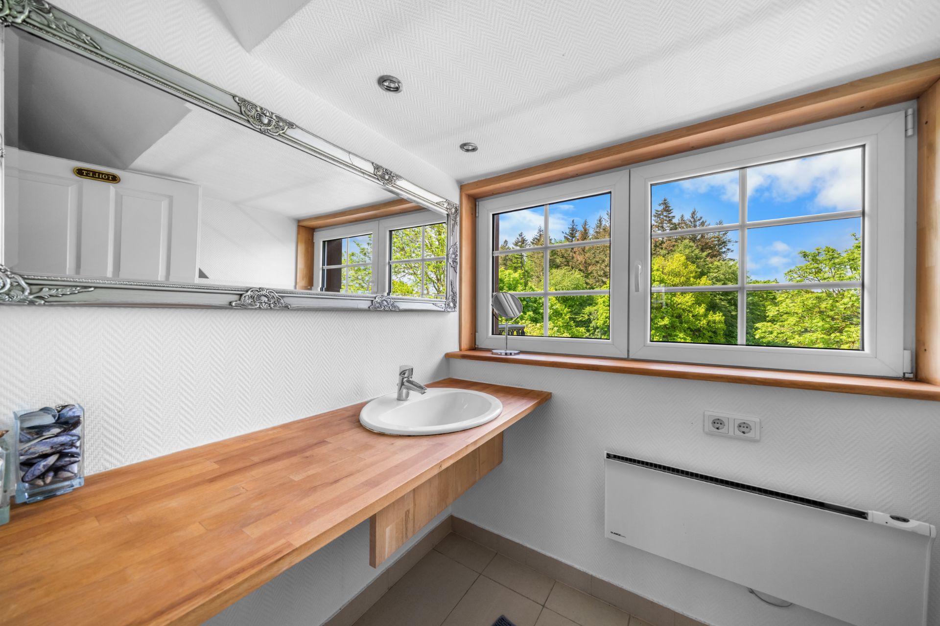 Helles Badezimmer mit großem Fenster, Spiegel und Holzwaschtisch mit Waschbecken.