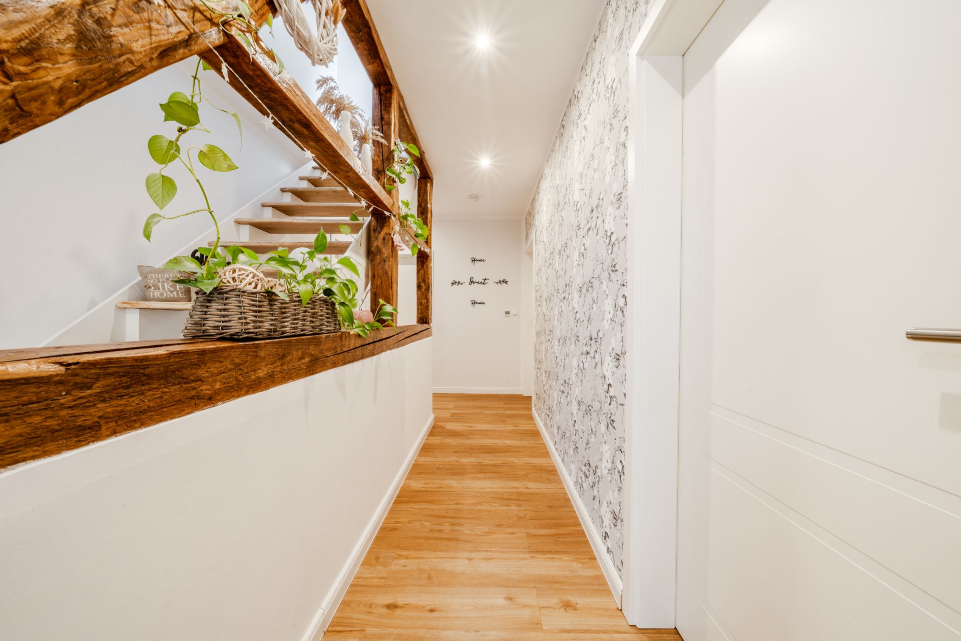 Heller Flur mit Holzboden, weißer Wand, Pflanzen auf einer hölzernen Brüstung und einer Treppe links.