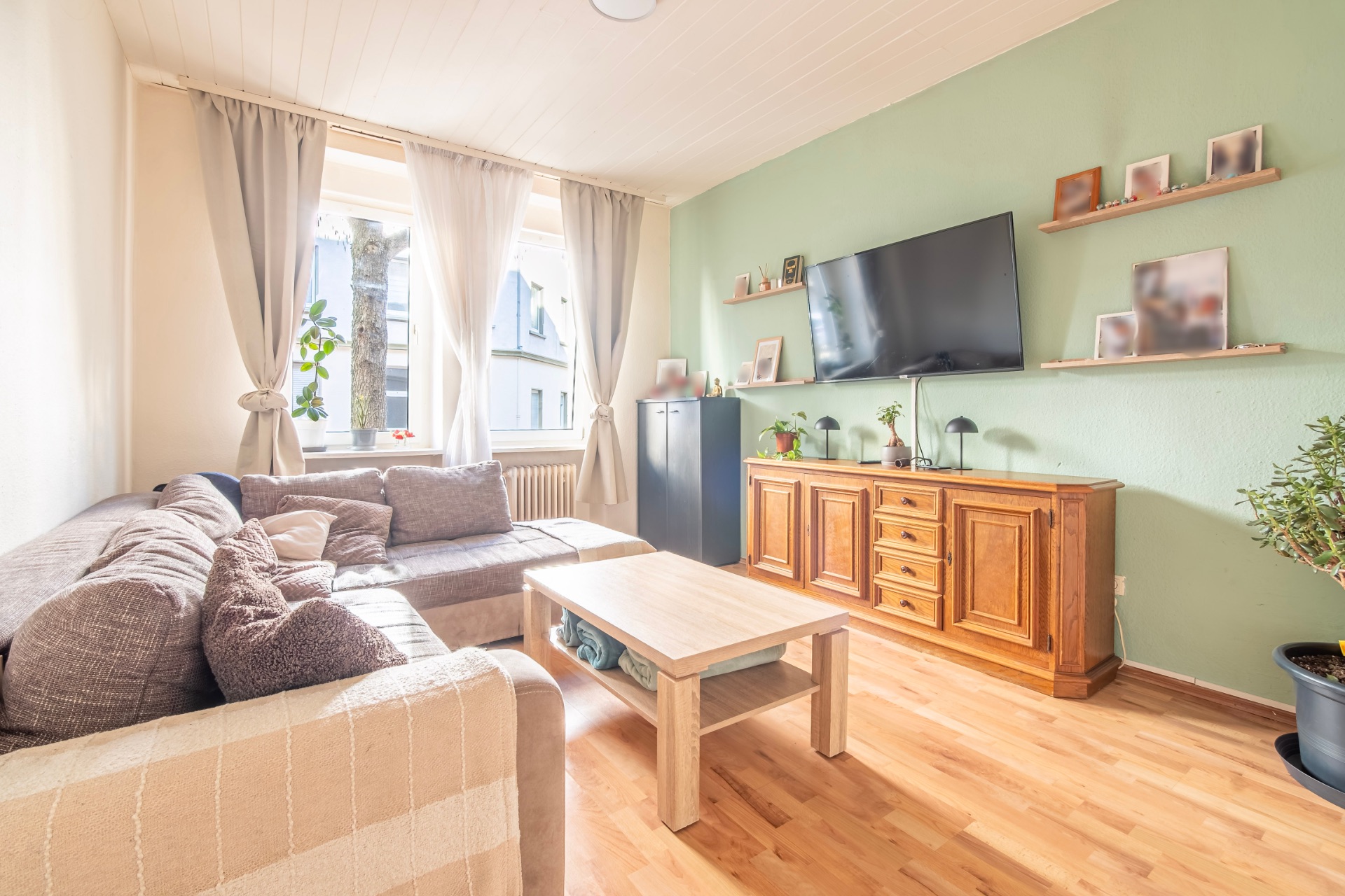 Helles Wohnzimmer mit Ecksofa, Couchtisch, Fernseher und Holzkommode auf Parkettboden.