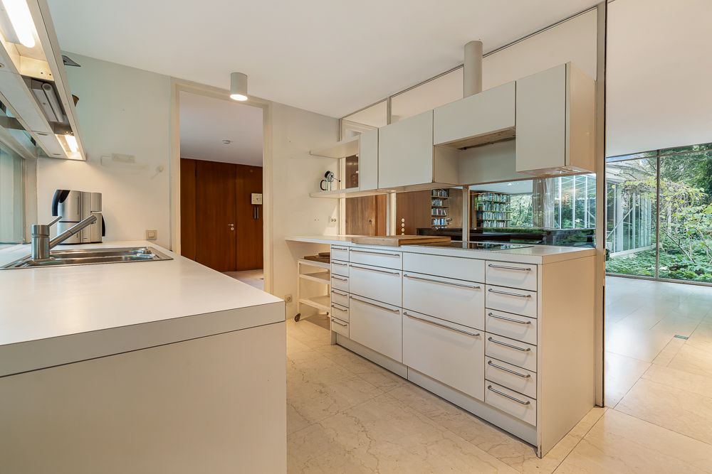 Moderne, helle Küche mit weißen Schränken, Spüle und großen Fenstern, Blick auf Garten.