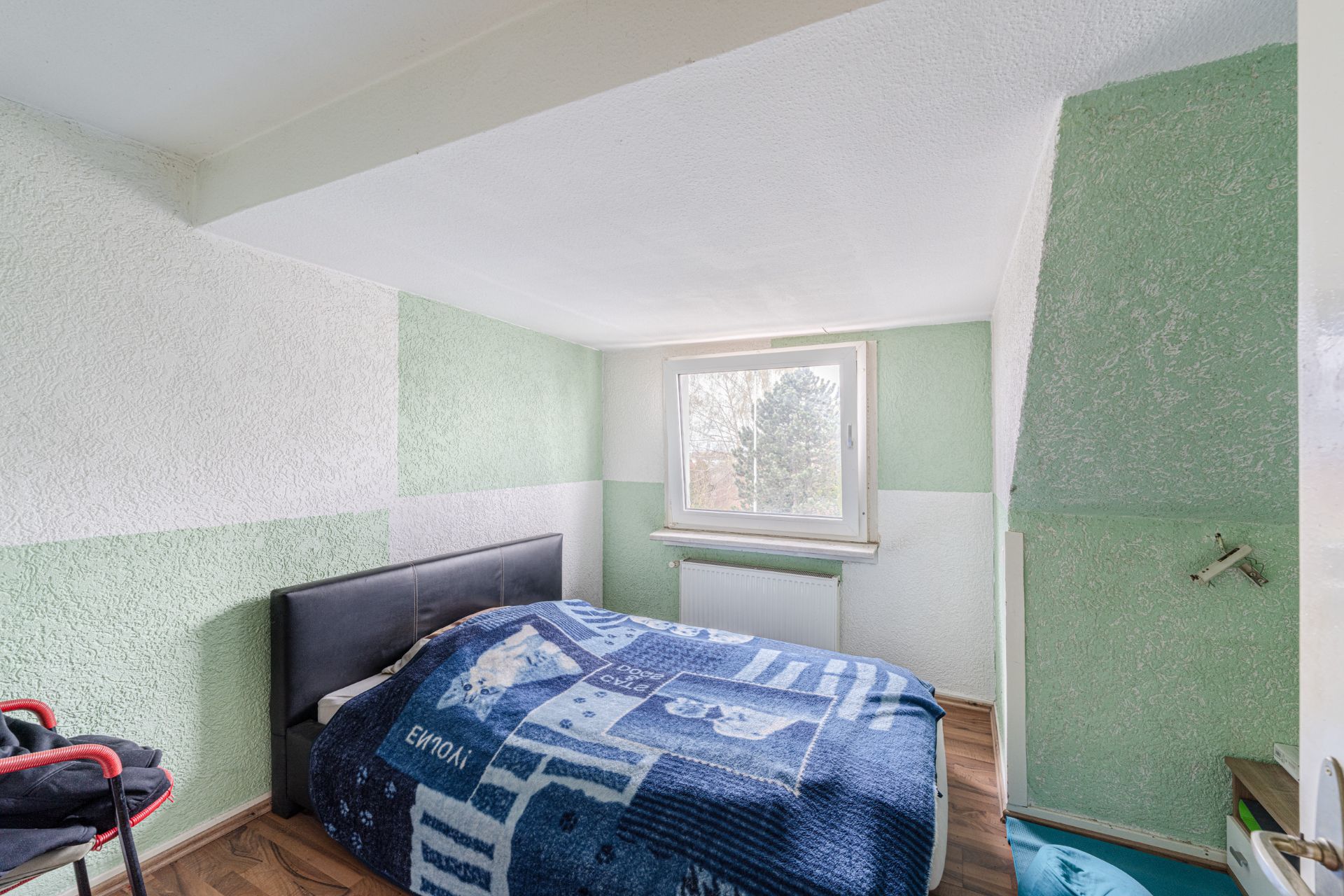 Kleines Schlafzimmer mit grün-weißen Wänden, Bett und Fenster mit Blick nach draußen.