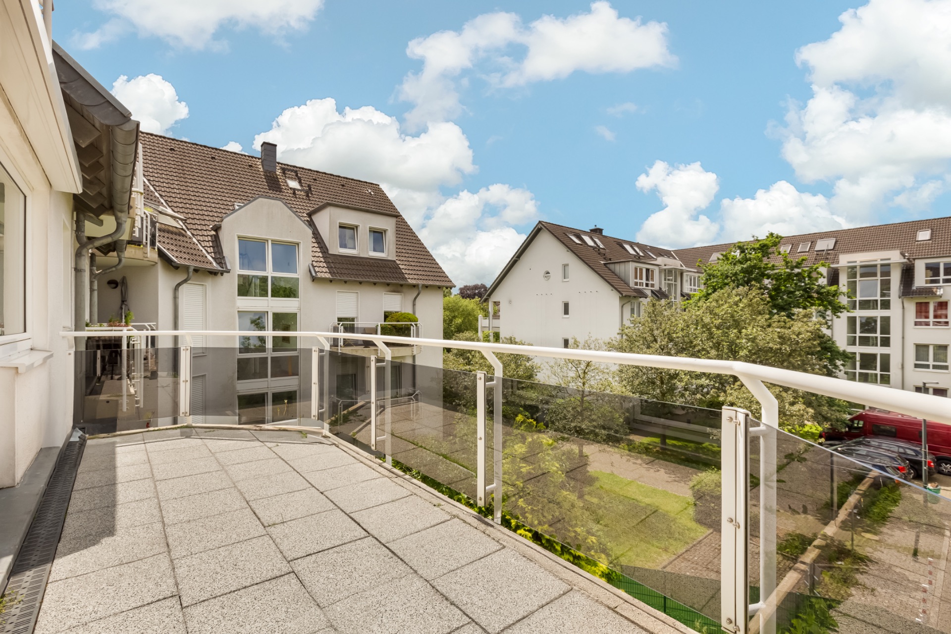 Balkon mit Glasgeländer und Blick auf Wohngebäude und Grünfläche.