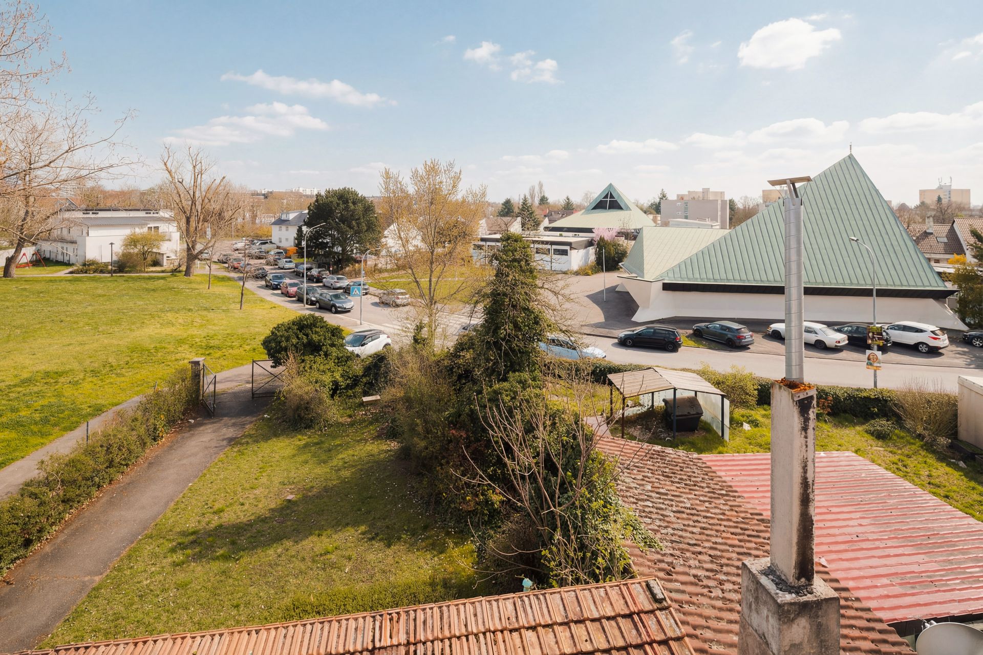 Blick von oben auf einen Garten mit Rasen, Weg und umliegender Straße mit Autos.