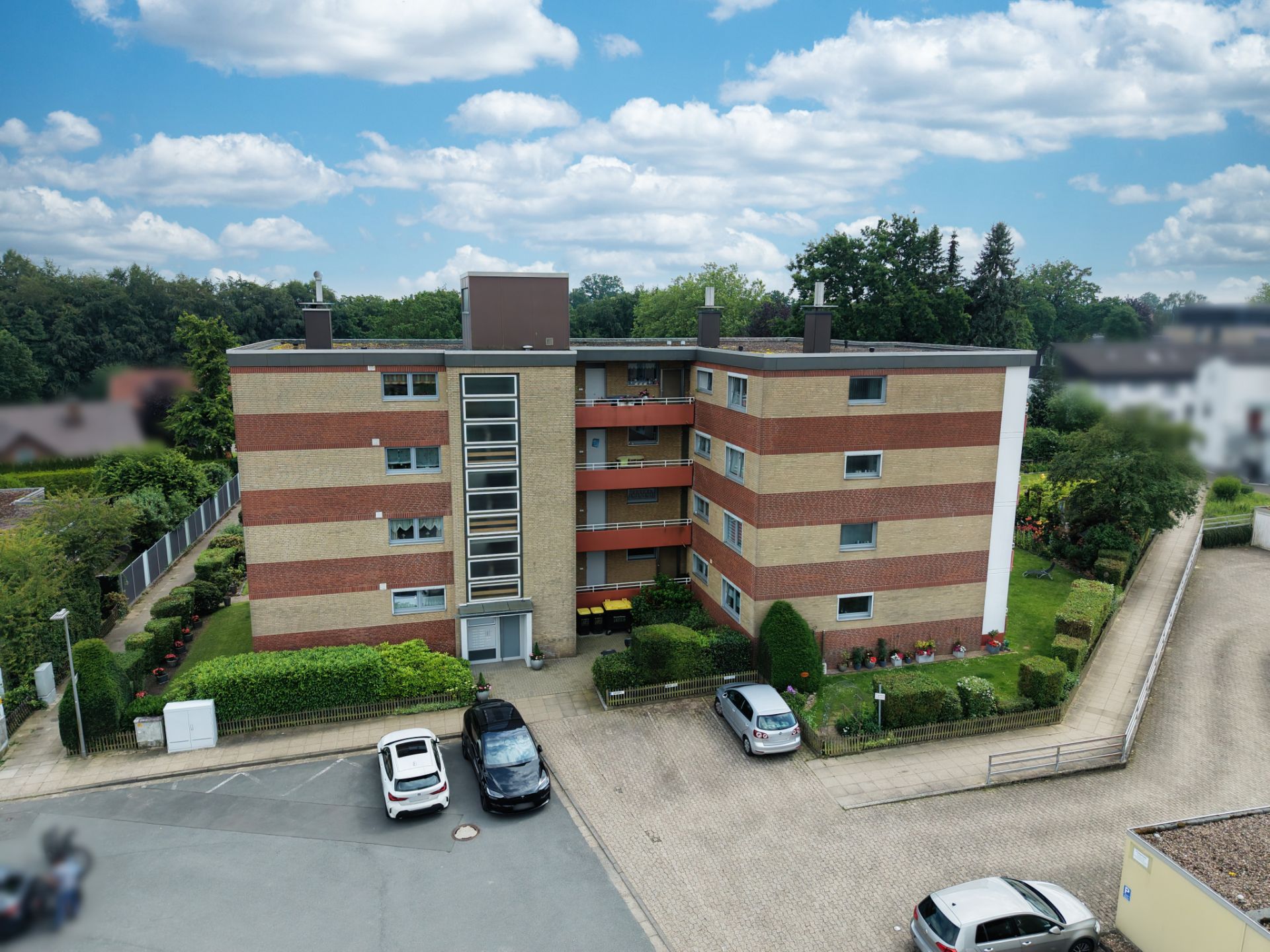 Dreistöckiges Wohnhaus mit Flachdach, Vorgarten und parkenden Autos vor dem Eingang.