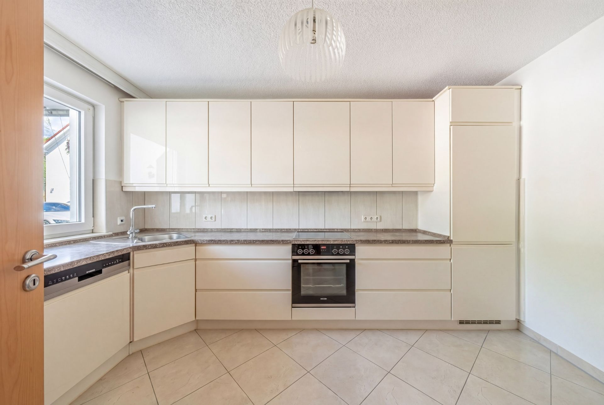 Helle, moderne Küche mit Einbauschränken, Herd, Spüle und Fenster.