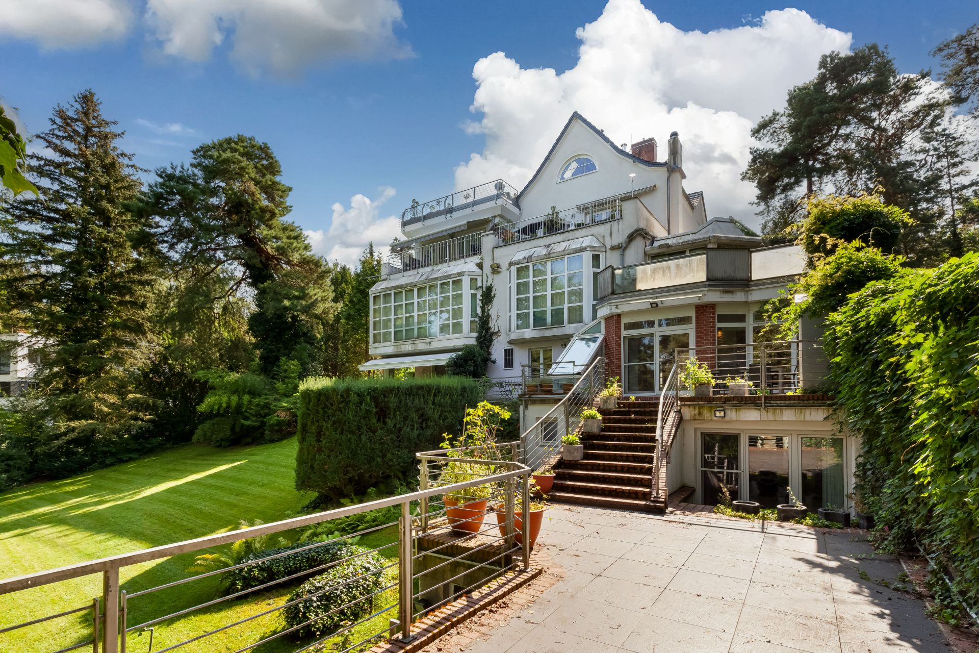Großes Wohnhaus mit mehreren Balkonen, Terrasse und gepflegtem Garten bei sonnigem Wetter.