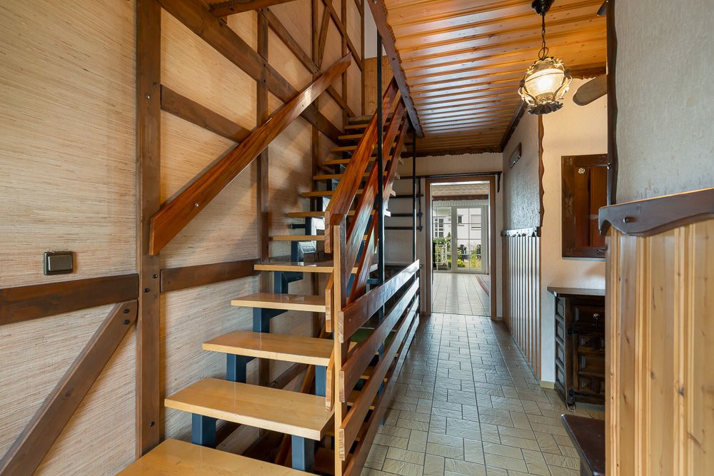 Flur mit offener Holztreppe, Holzdecke und Blick auf einen Ausgang zum Garten.