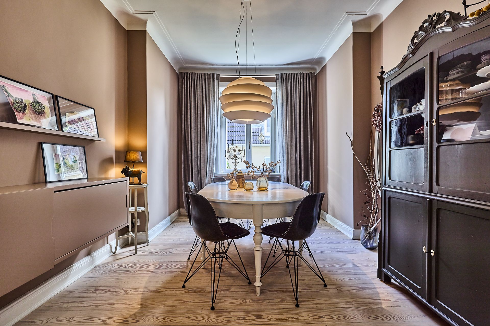 Esszimmer mit rundem Tisch, vier Stühlen, Hängelampe und großem Schrank am Fenster.