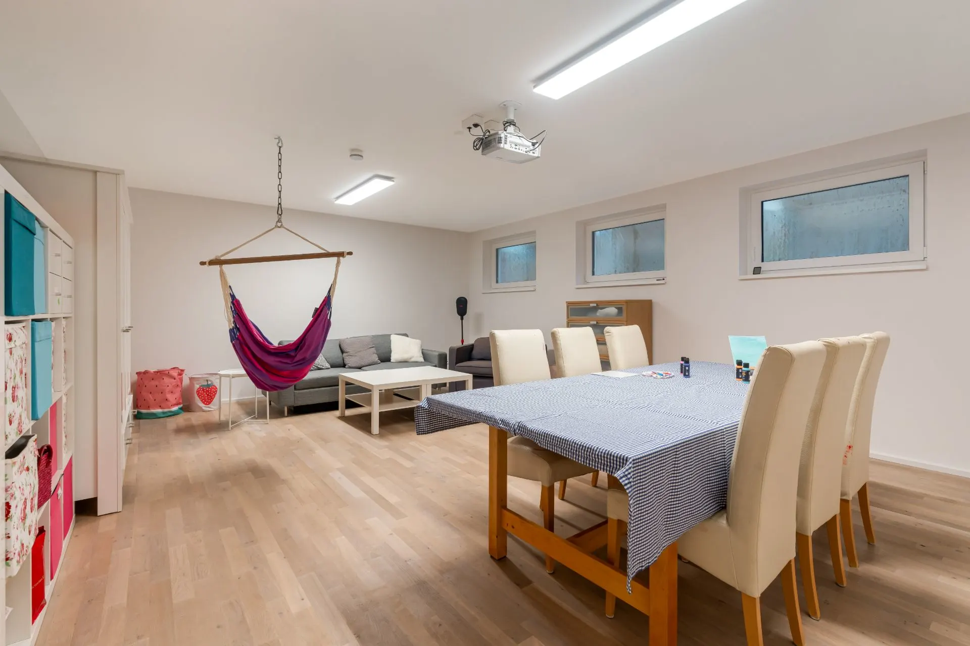 Helles Wohnzimmer mit Essbereich, Hängesessel, Sofa, Esstisch und Stühlen auf Holzfußboden.