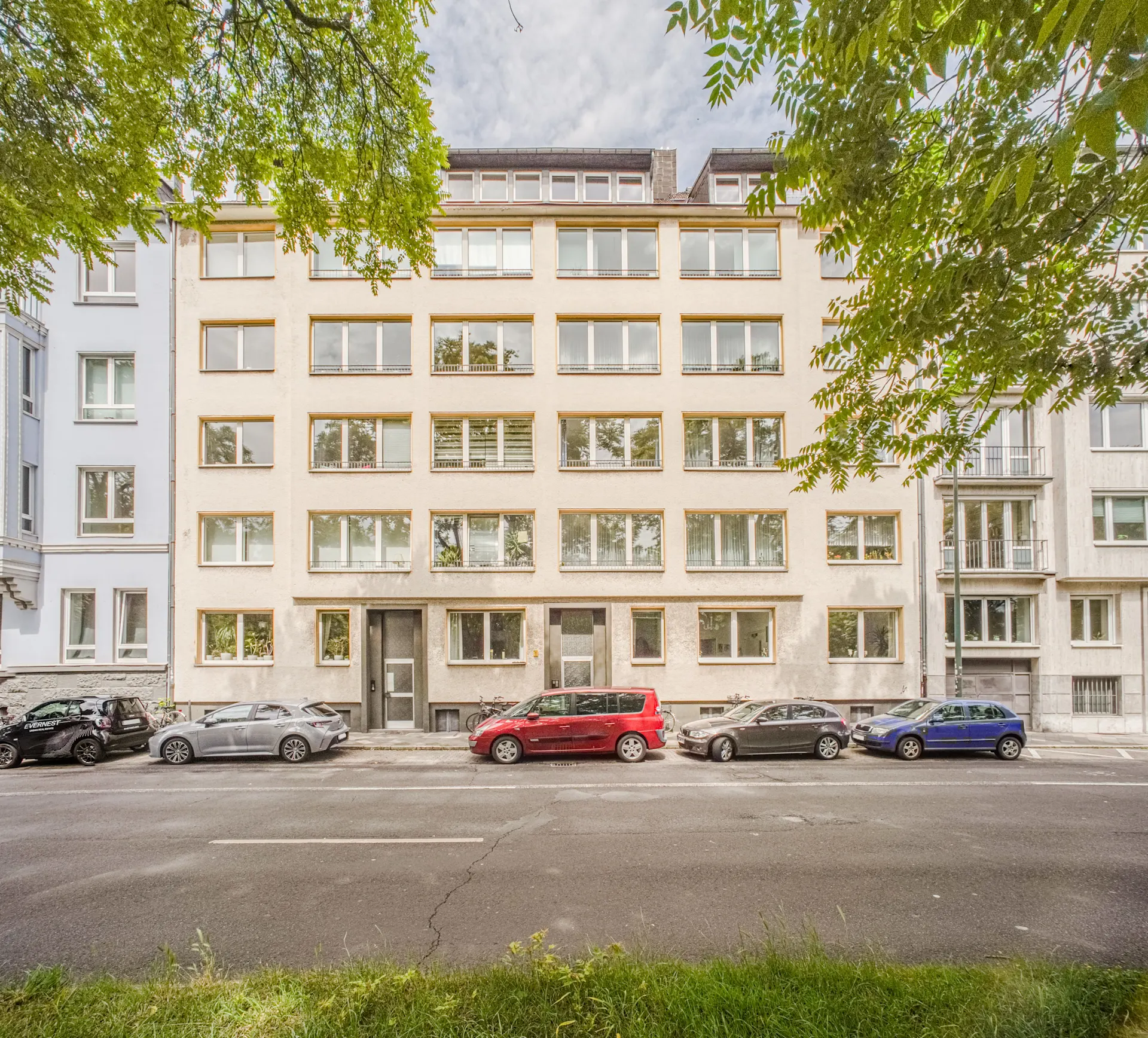Mehrstöckiges Wohngebäude mit vielen Fenstern und Autos, die auf der Straße davor parken.