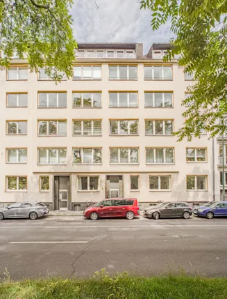 Mehrstöckiges Wohngebäude mit vielen Fenstern und Autos, die auf der Straße davor parken.