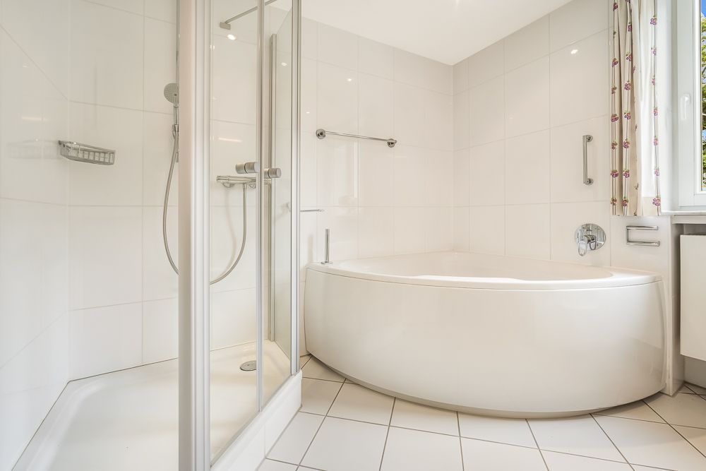 Modernes Badezimmer mit Eckbadewanne und Duschkabine, weiße Fliesen an Wand und Boden.
