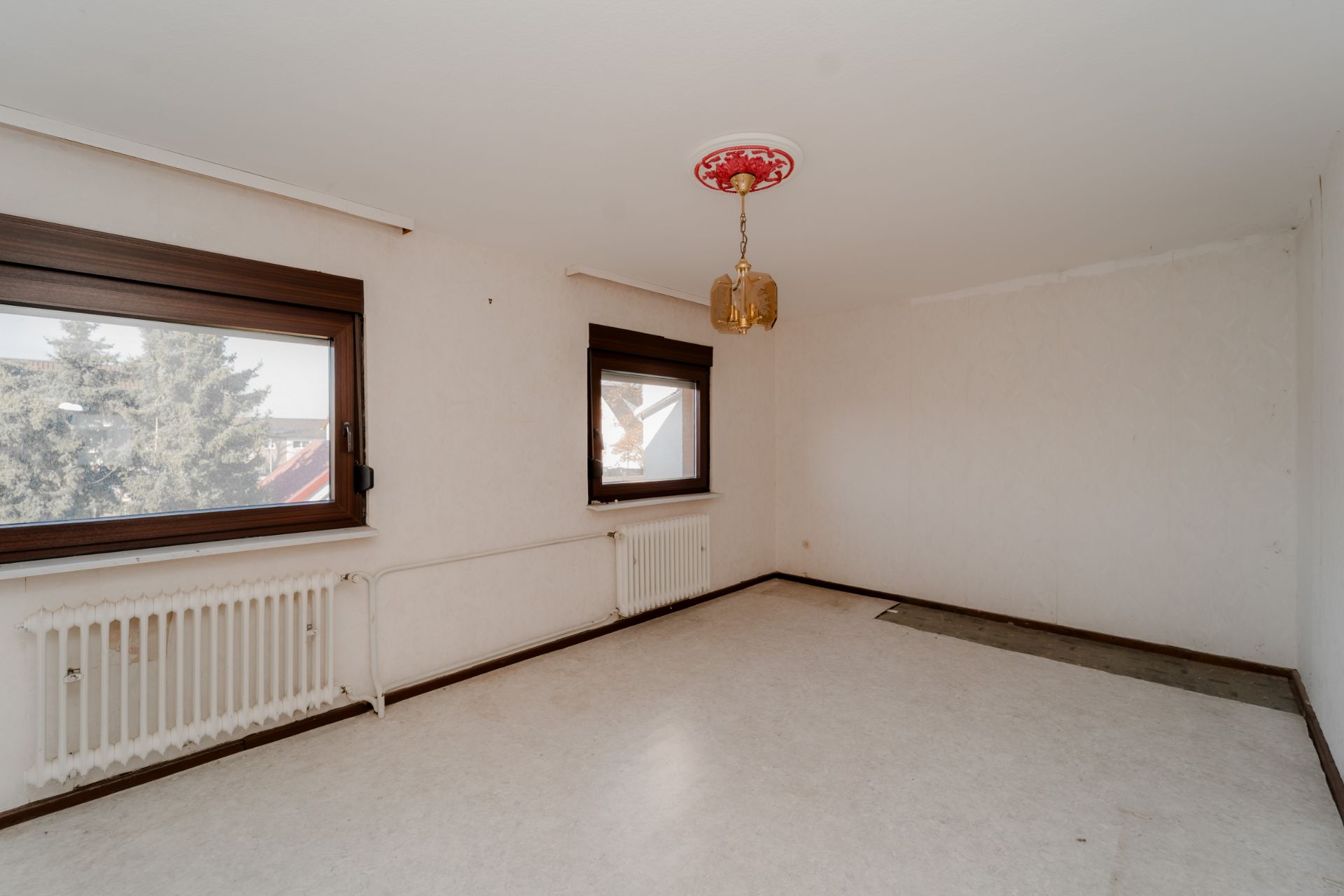Leerer Raum mit zwei Fenstern, Heizung und Lampe an der Decke.