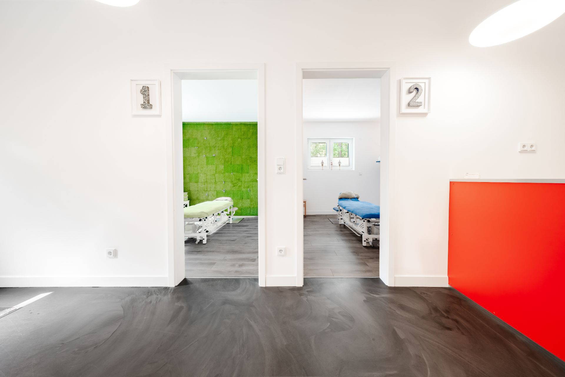 Zwei nebeneinanderliegende Zimmer mit nummerierten Türen, eines mit grüner, eines mit weißer Wand.
