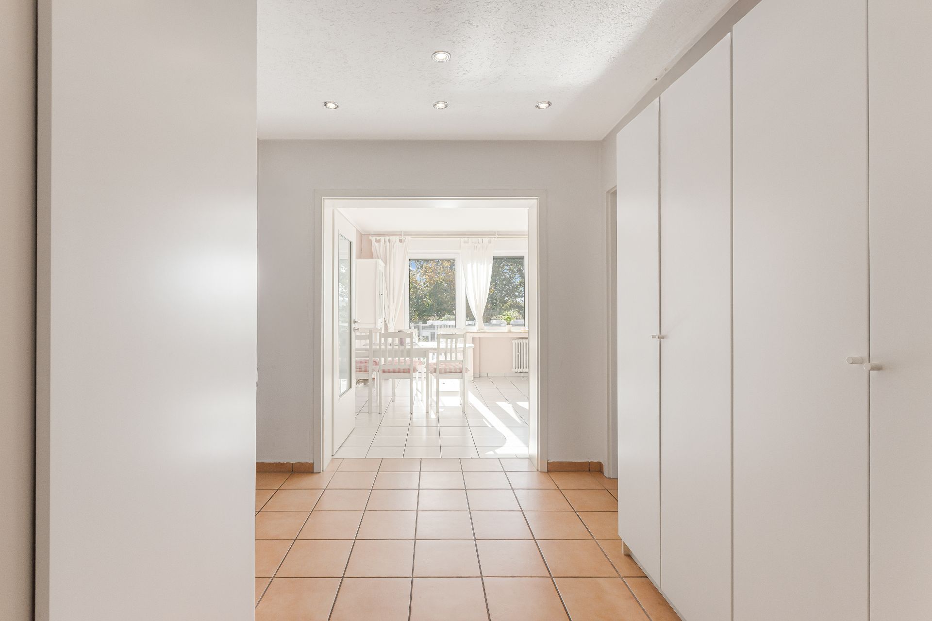 Heller Flur mit Einbauschränken und Blick in ein Esszimmer mit großen Fenstern.