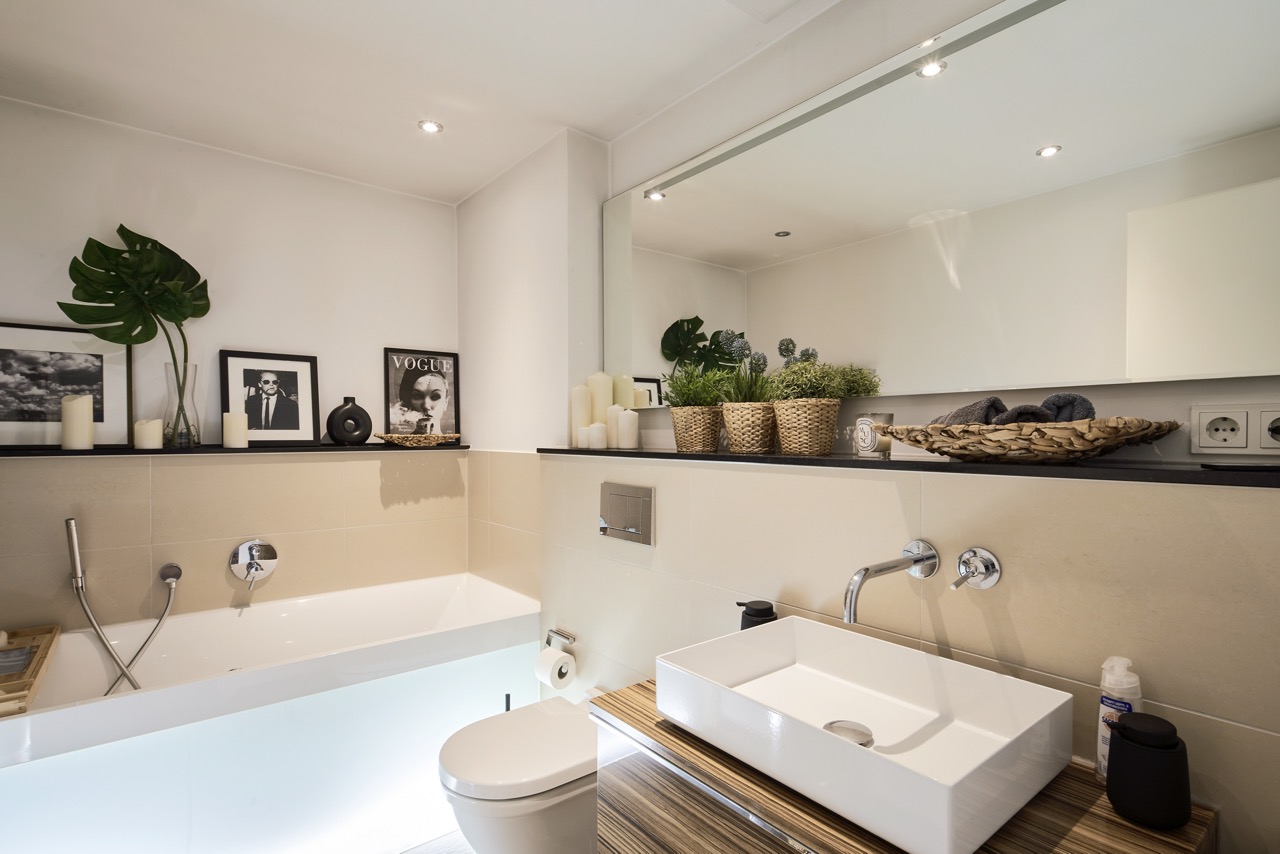 Modernes Badezimmer mit Badewanne, Waschbecken, Dekobildern, Pflanzen und großem Spiegel.