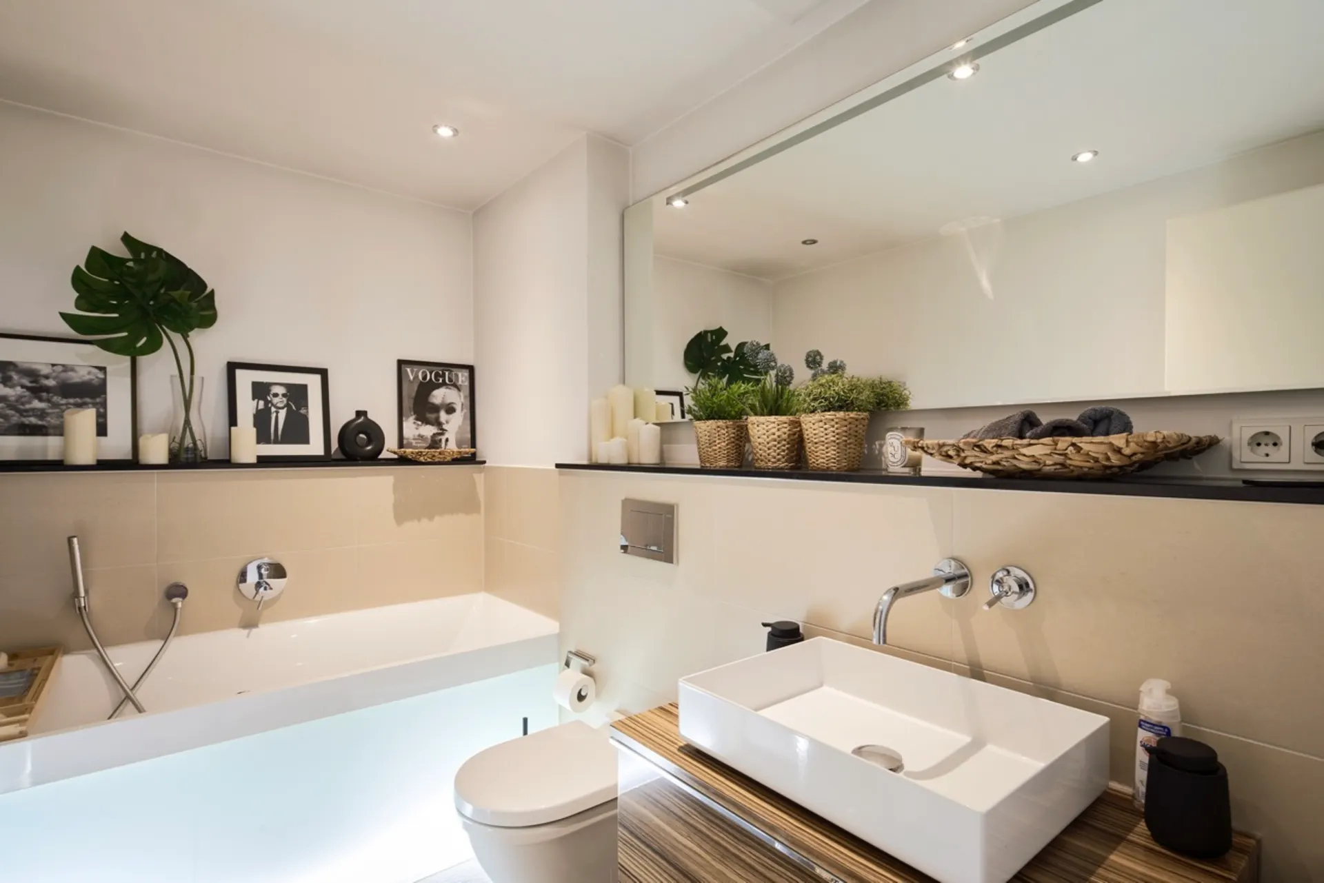 Modernes Badezimmer mit Badewanne, Waschbecken, Dekobildern, Pflanzen und großem Spiegel.