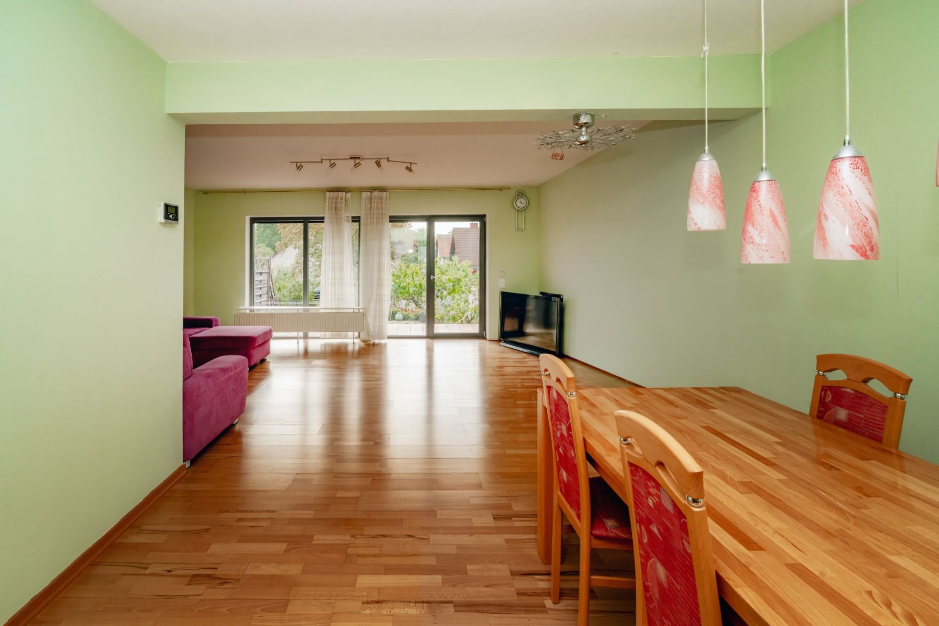 Wohnzimmer mit Holzboden, Essbereich, roten Stühlen, Sofa und großen Fenstern mit Blick nach draußen.