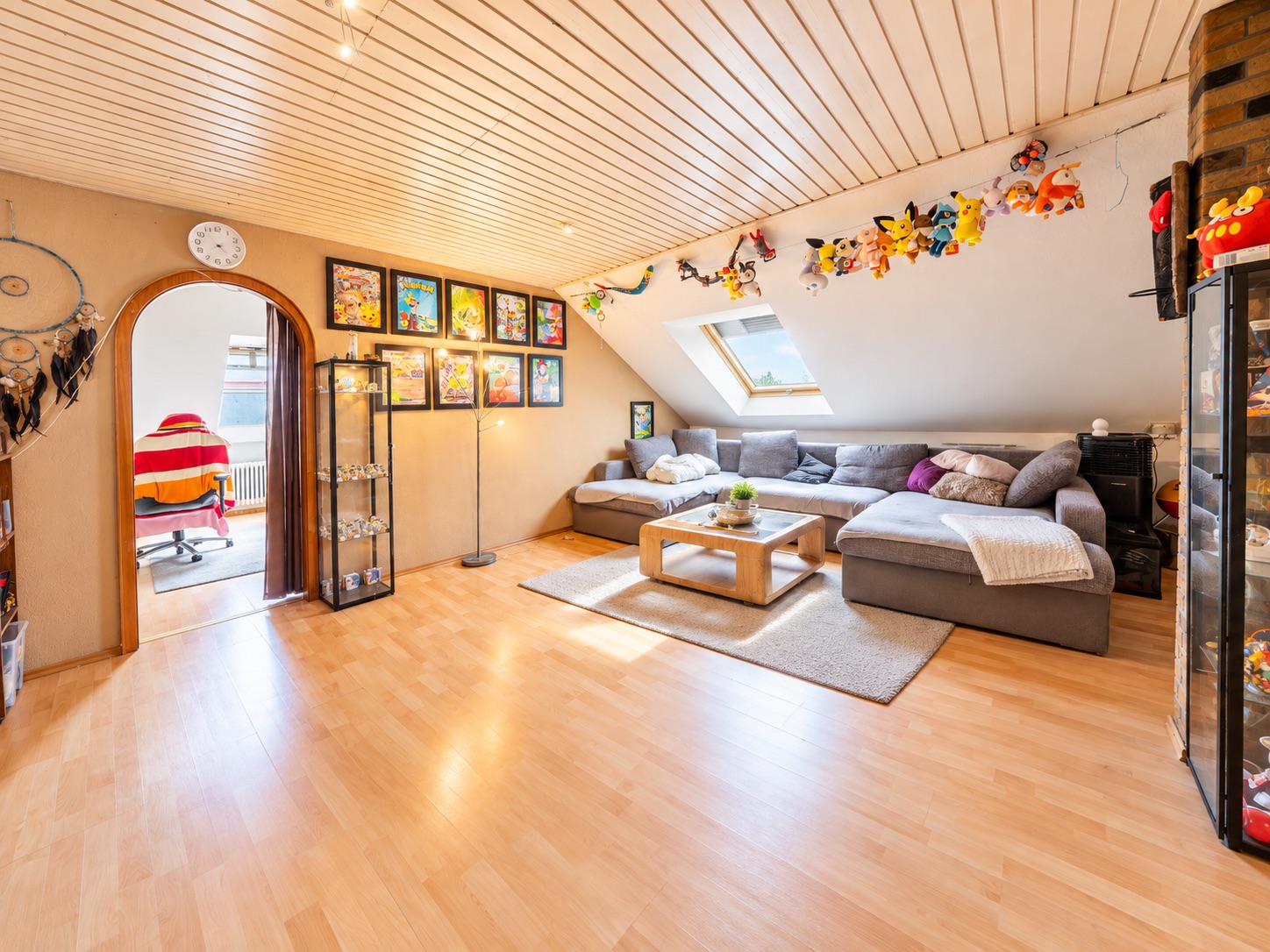 Helles Dachwohnzimmer mit großem Ecksofa, Couchtisch, Spielzeug und Bildern an der Wand.