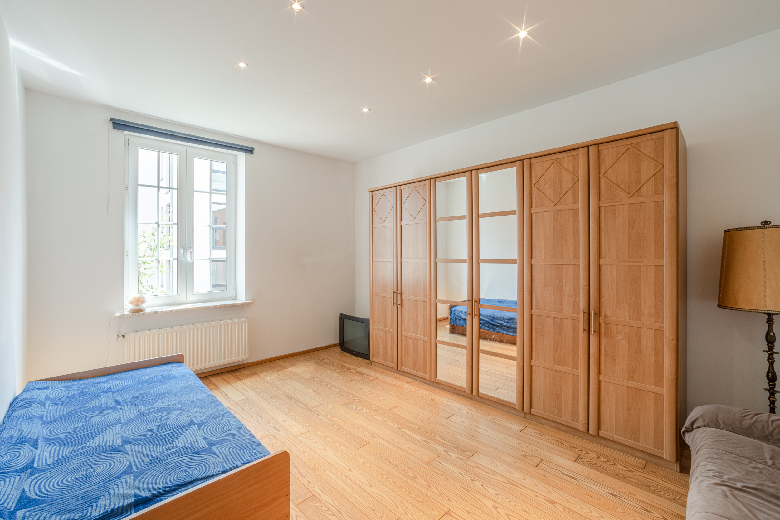 Helles Schlafzimmer mit Holzboden, großem Kleiderschrank, Bett und Fenster.