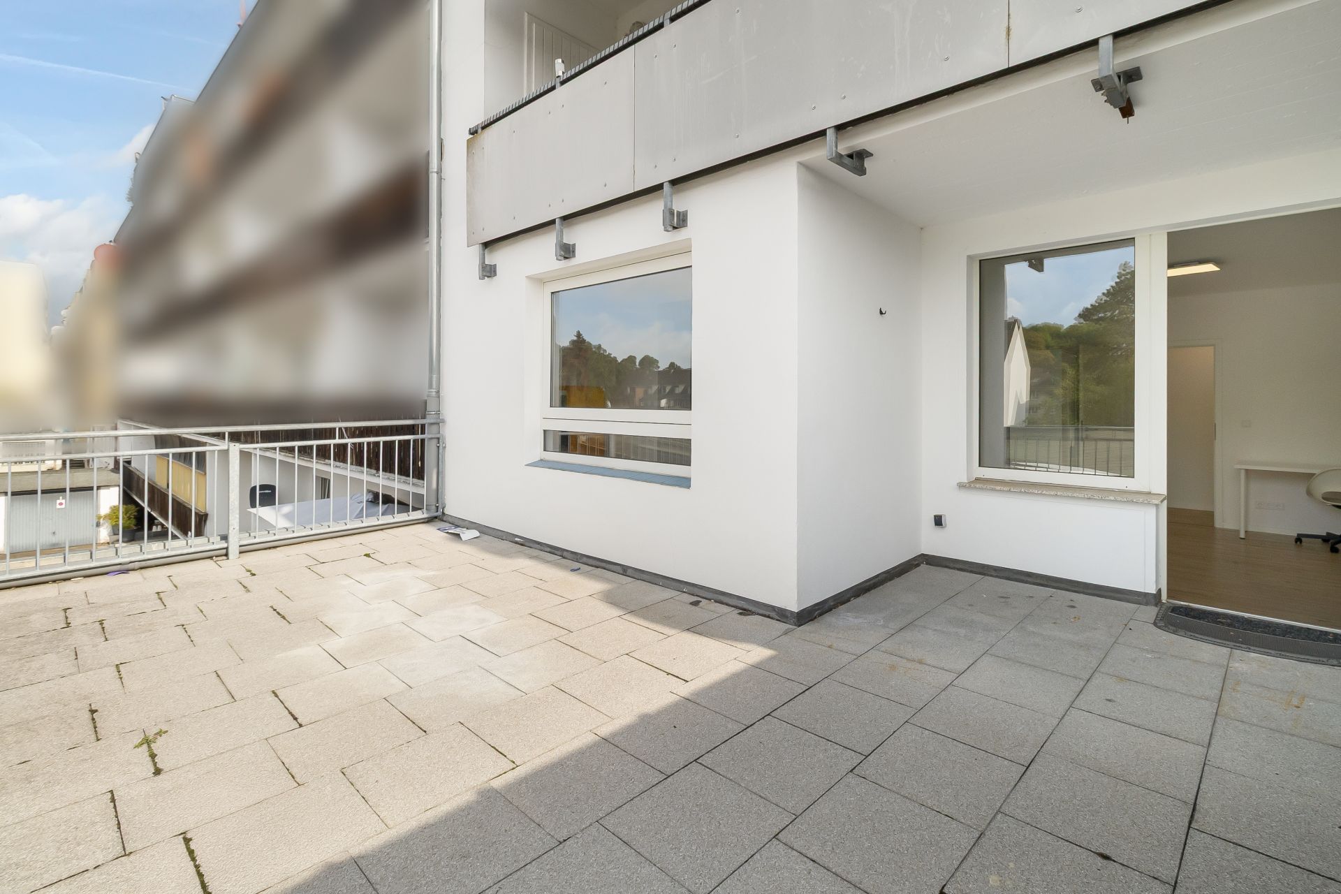 Große Terrasse mit hellen Bodenplatten und Zugang zu einer Wohnung mit Fenstern und Glastür.